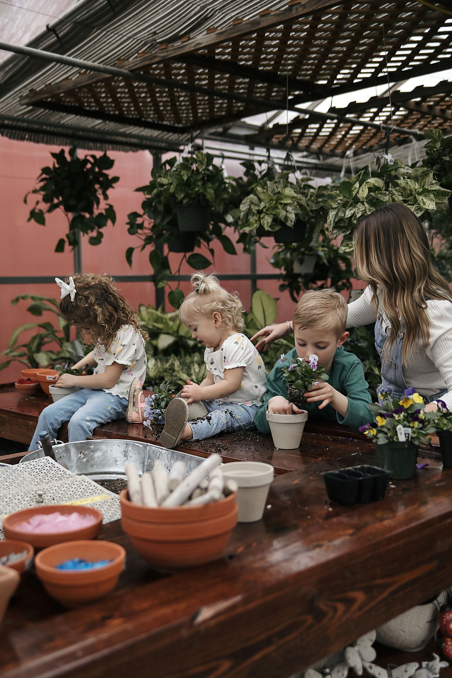 Children gather around a wooden table during a hands-on gardening or planting activity with terracotta pots and materials.