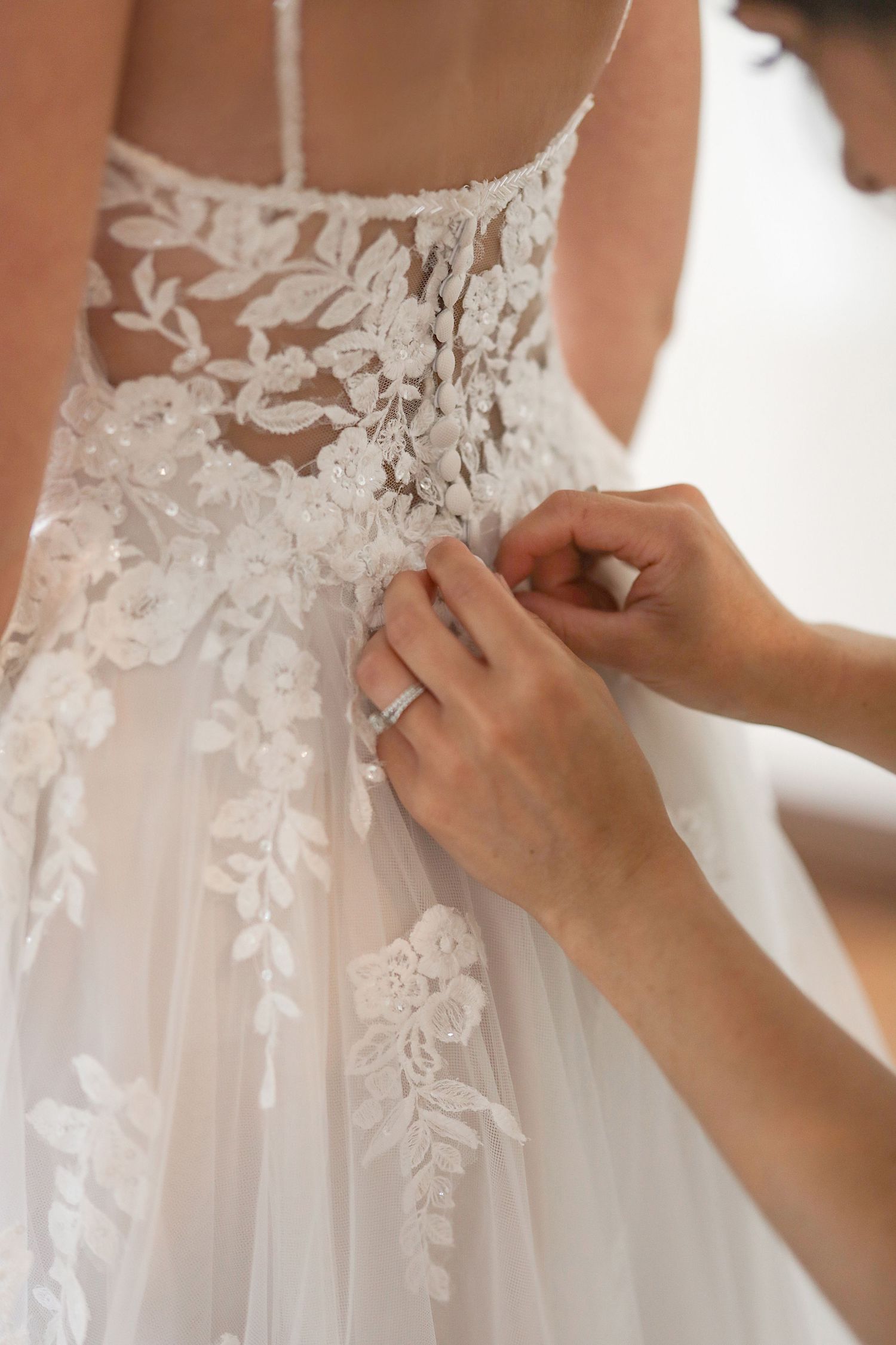 Close-up detail of delicate lace appliques being adjusted on the back of a white wedding gown. Cleveland wedding photographer.