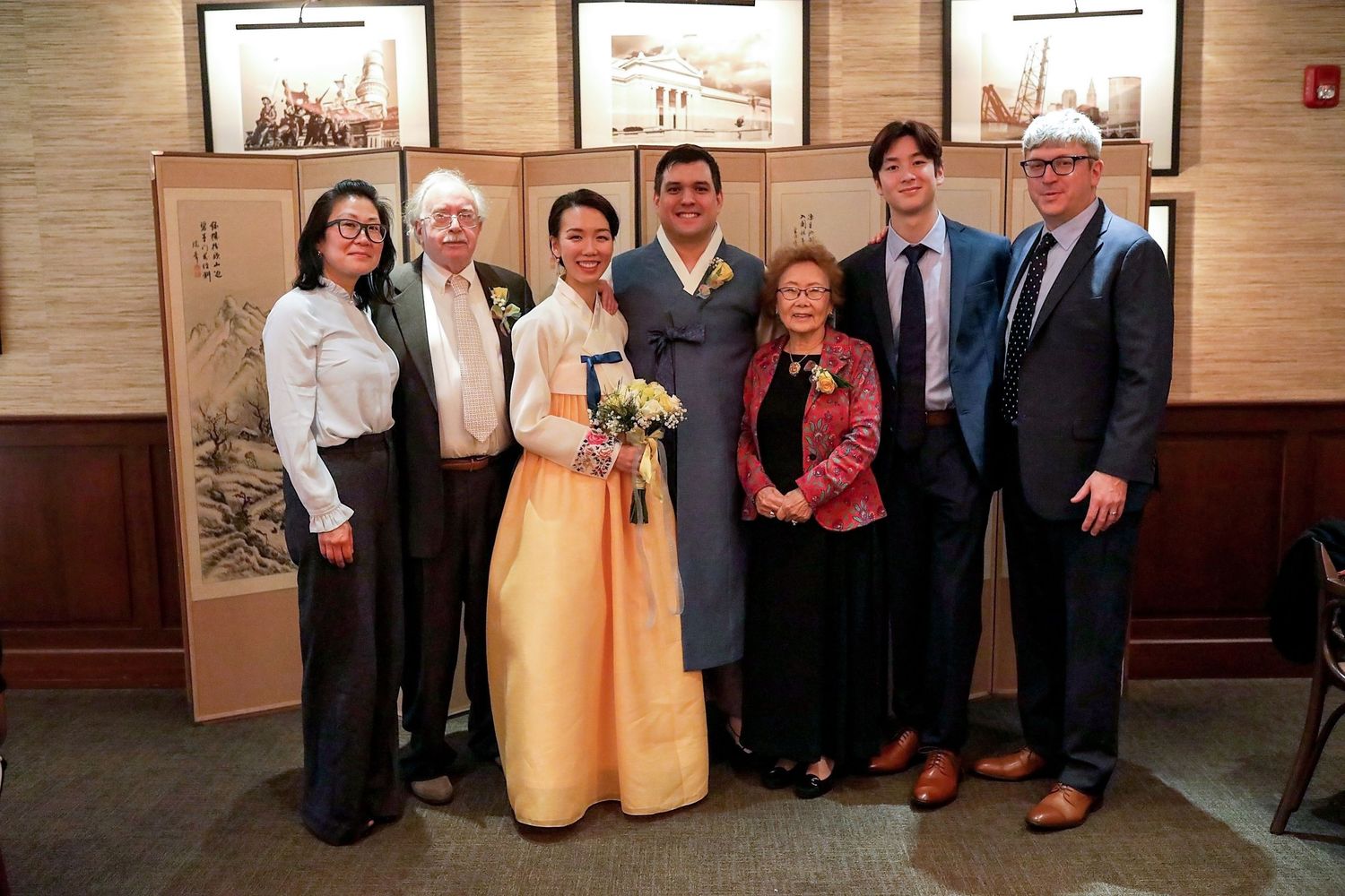 Group of people standing together at a formal event with wood-paneled walls and framed artwork in the background.