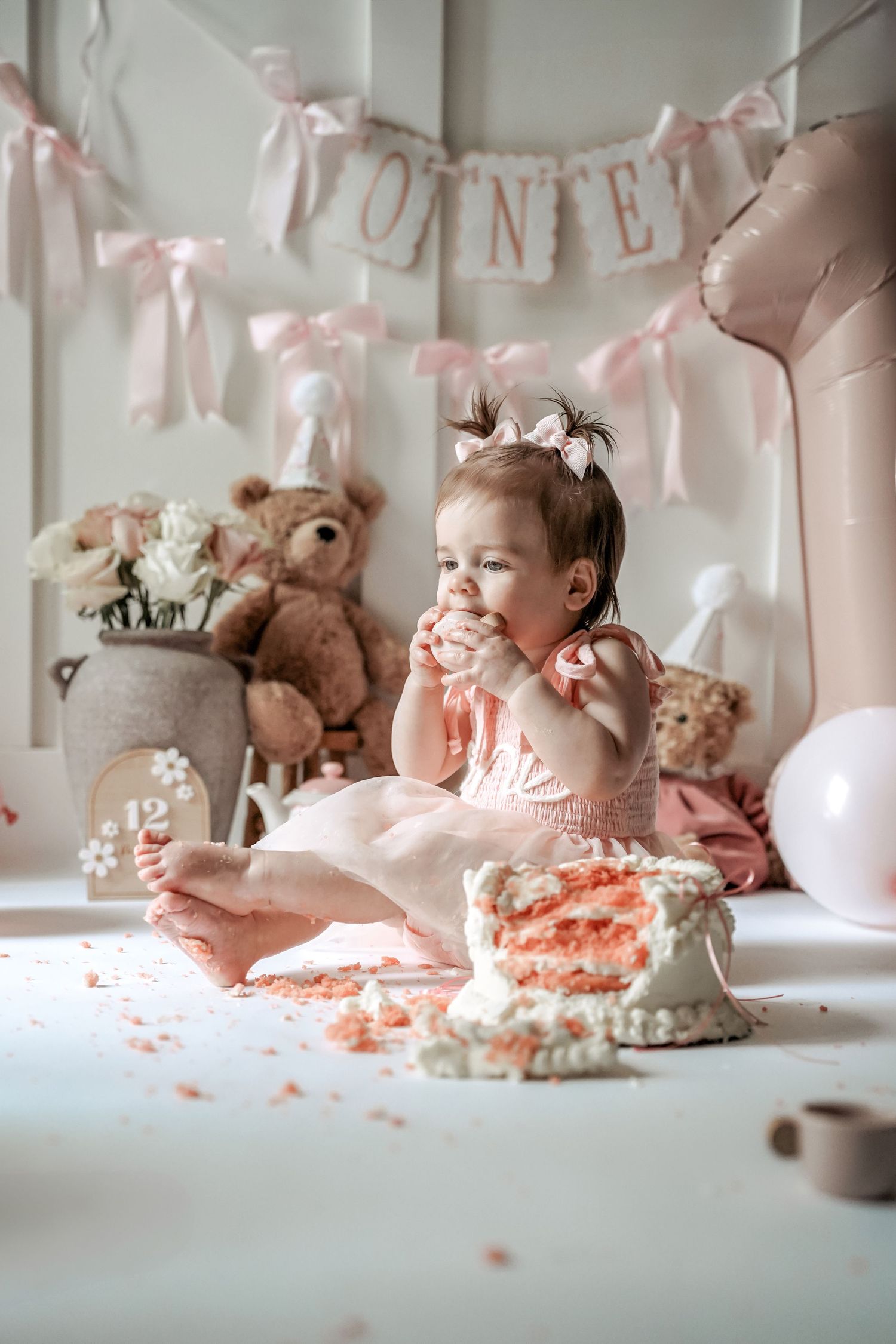 A cake smash photo series with pink decorations and stuffed animals showing a baby enjoying their first birthday celebration.
