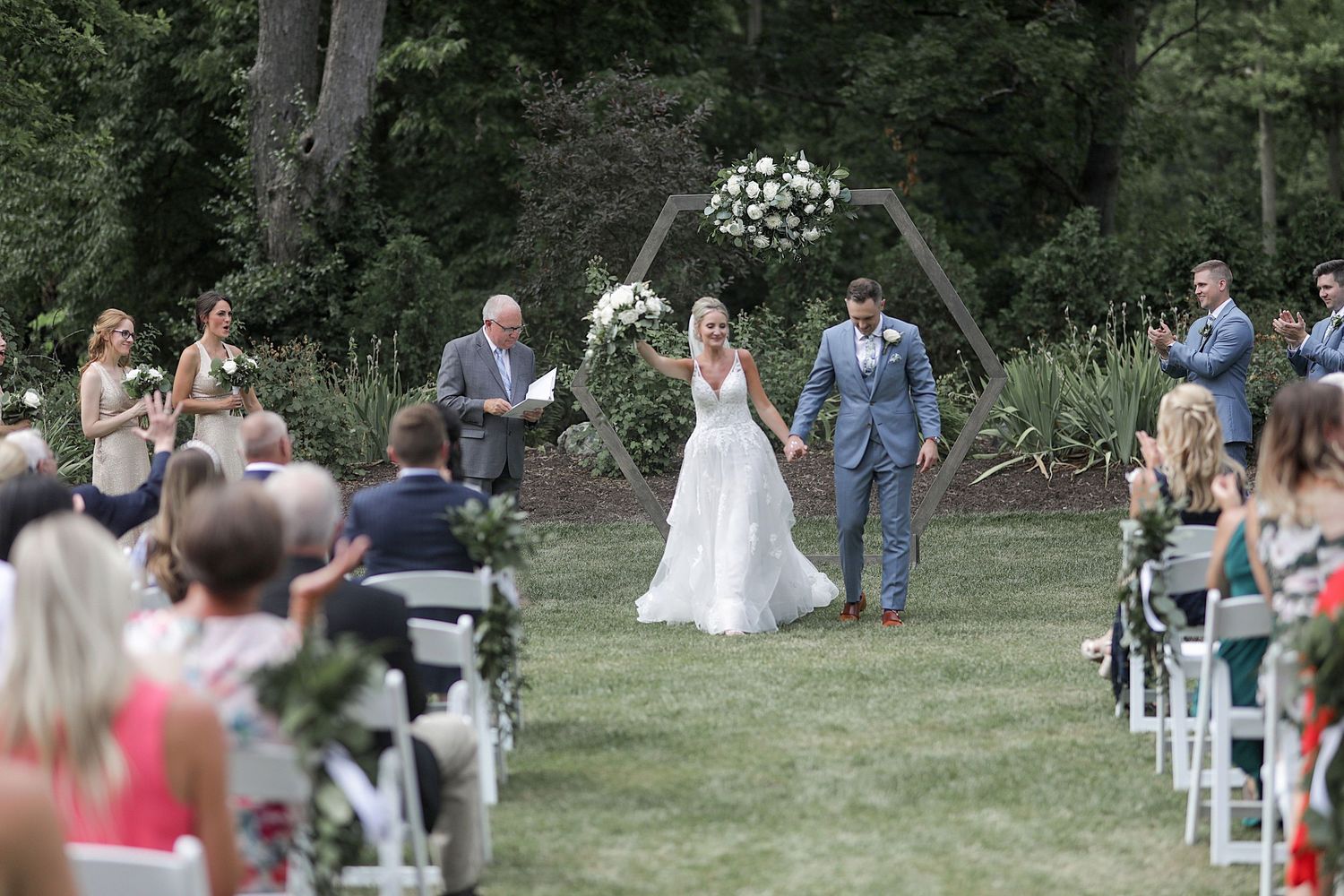 Wedding ceremony setup in an outdoor garden with white chairs and guests seated on the lawn.