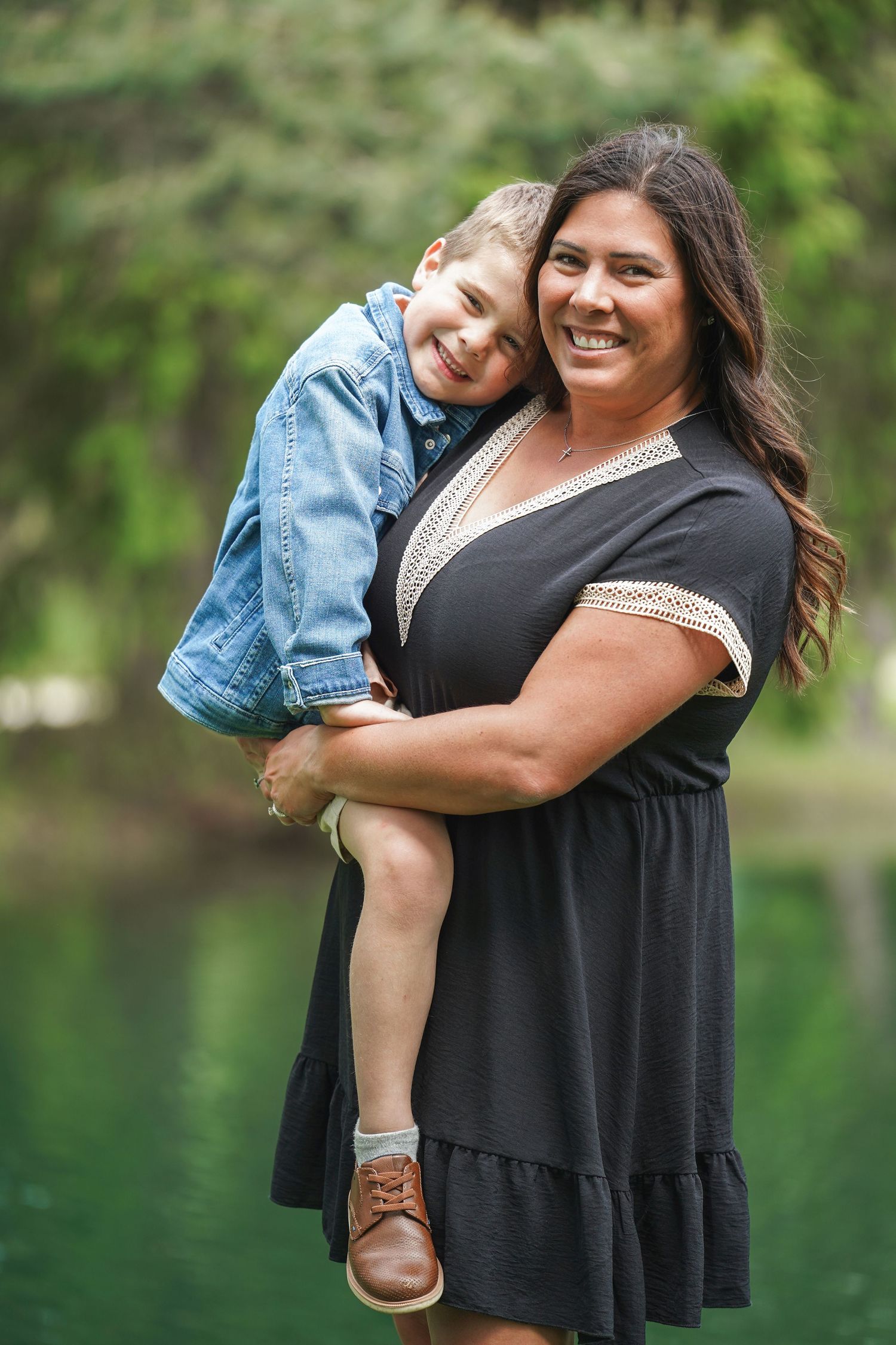 A close-knit pair share joyful embraces and laughter against a serene outdoor backdrop by the water.