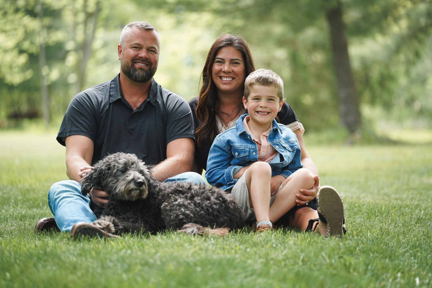 Family and their schnauzer dog relaxing together on green grass in a sunny park setting.