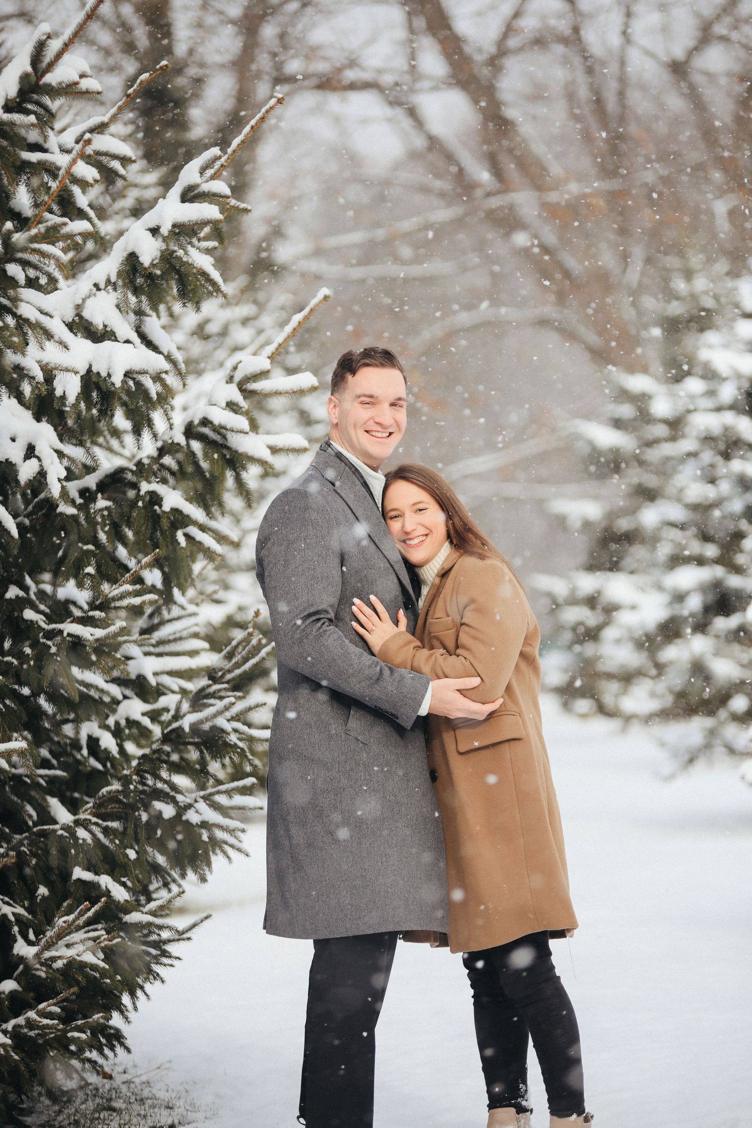 A couple shares joyful moments together in a snowy winter setting surrounded by snow-covered evergreen trees.