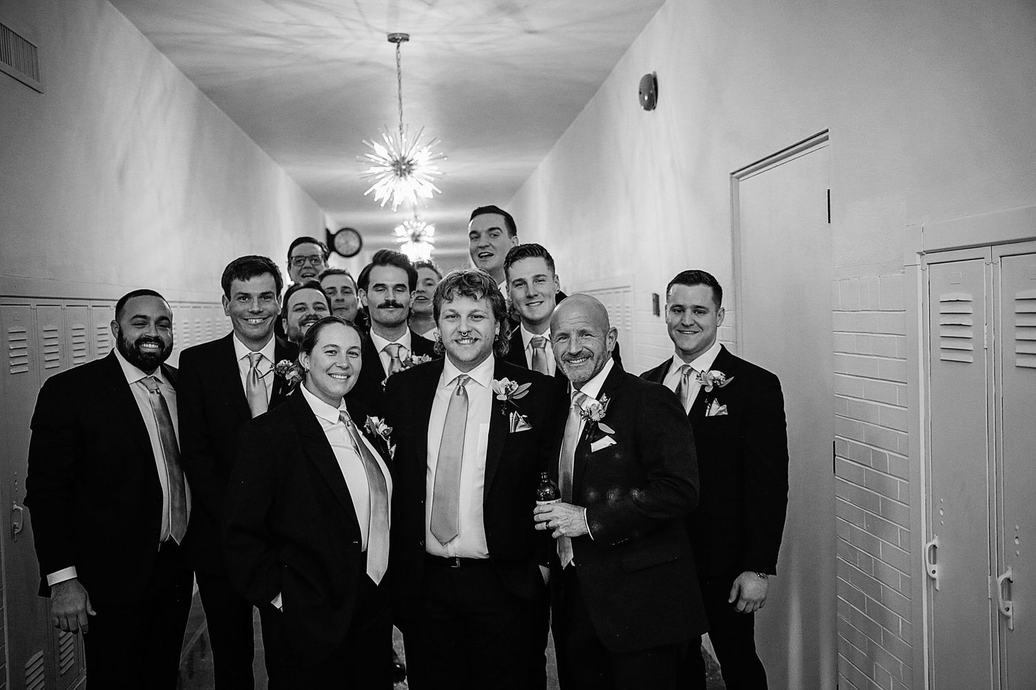 Black and white panoramic photo of a group celebrating in a hallway with lockers visible in the background.
