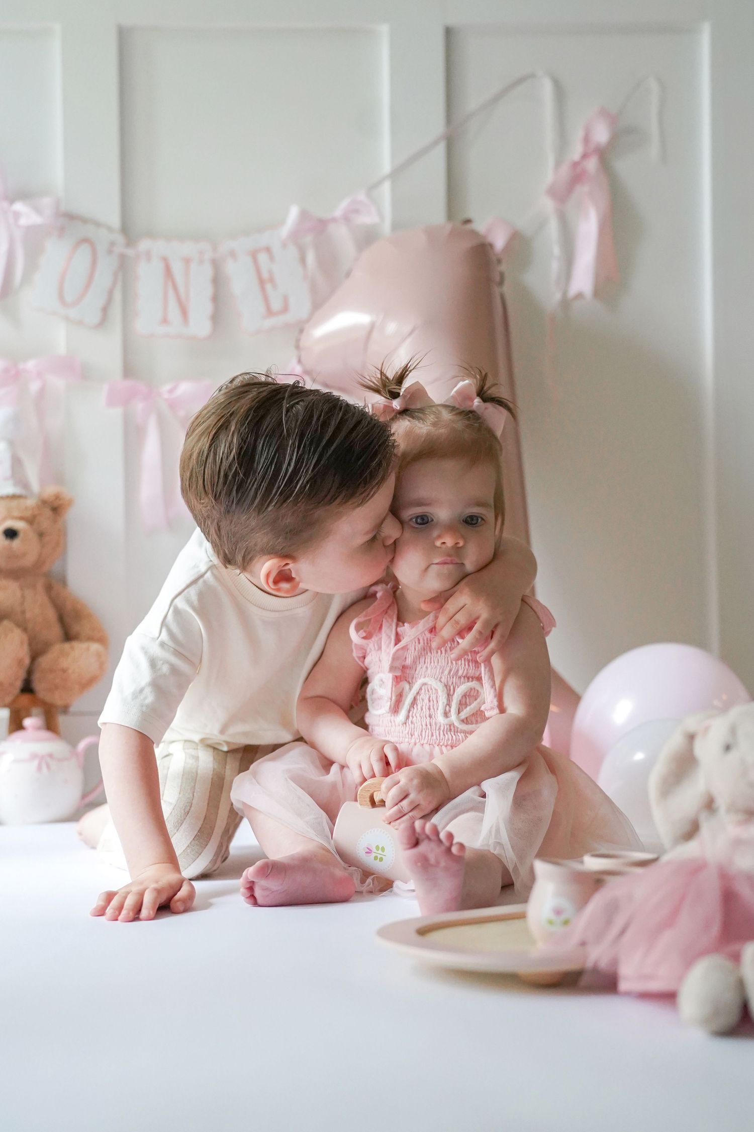 Pink birthday party setup with decorative banner, balloons, and stuffed animals creating a soft, romantic celebration scene.