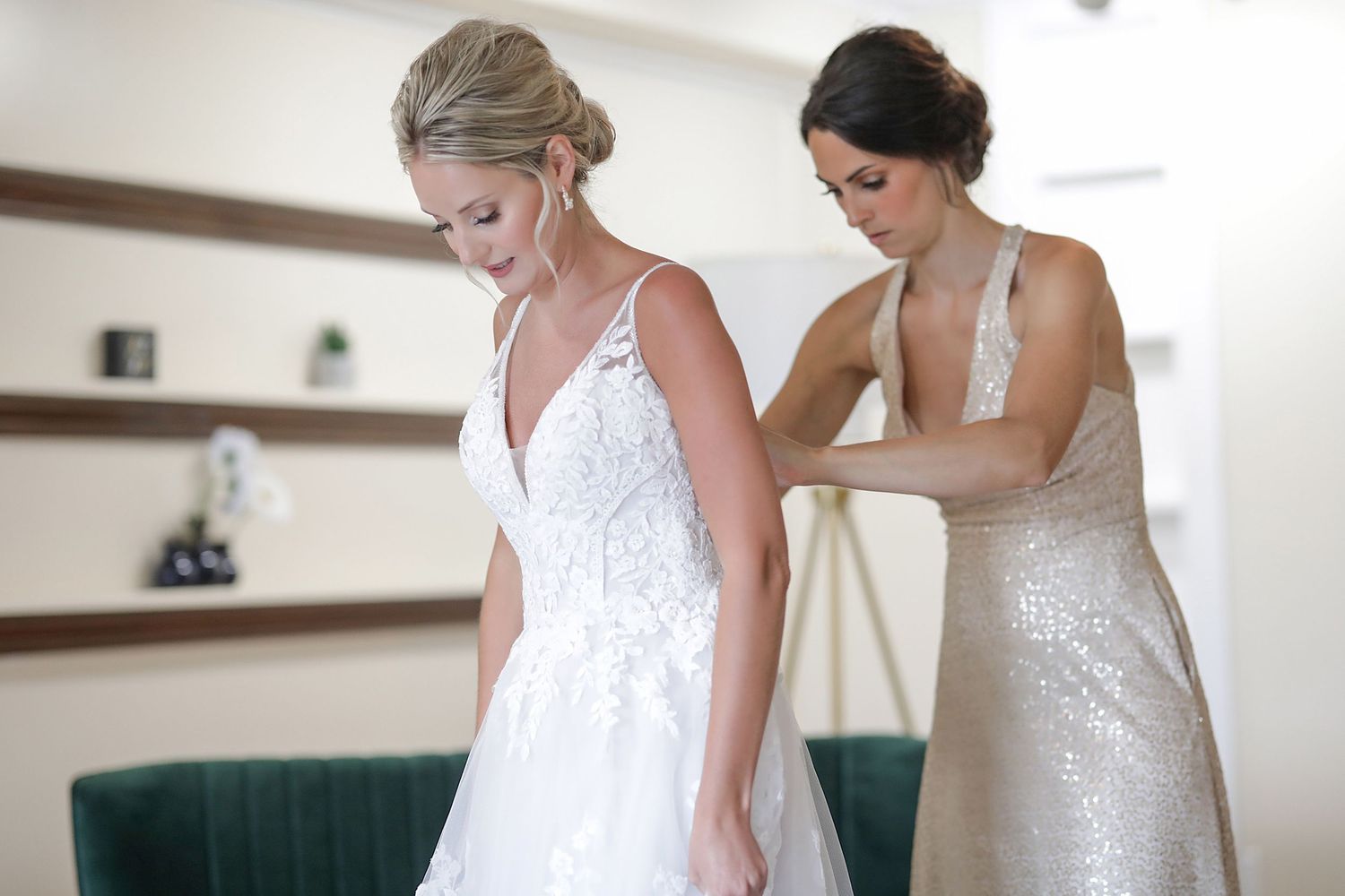 Two people helping with a white wedding dress fitting in a bright interior space.