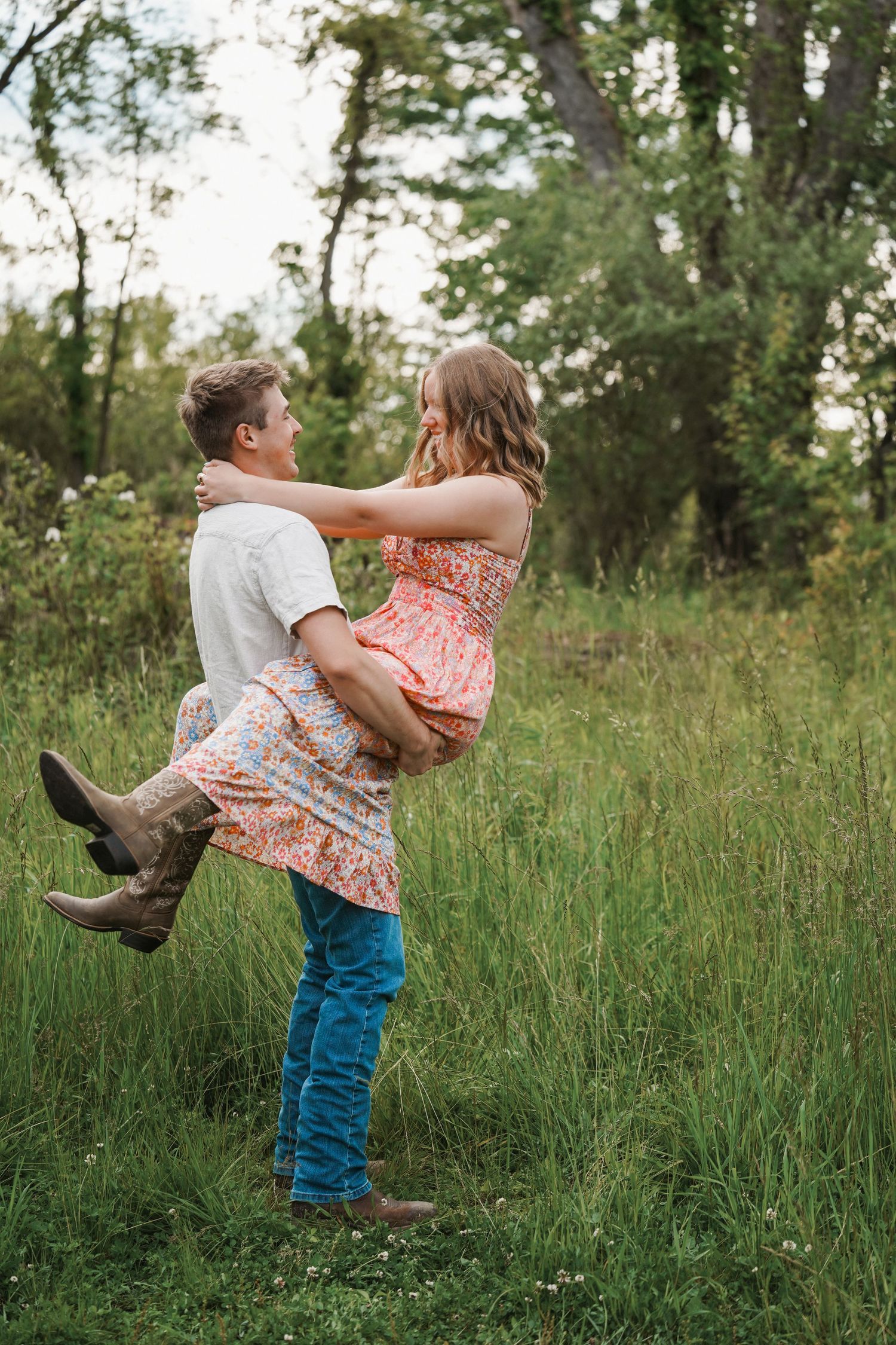 Two people playfully spinning and dancing together in a tall grass field on a sunny afternoon.