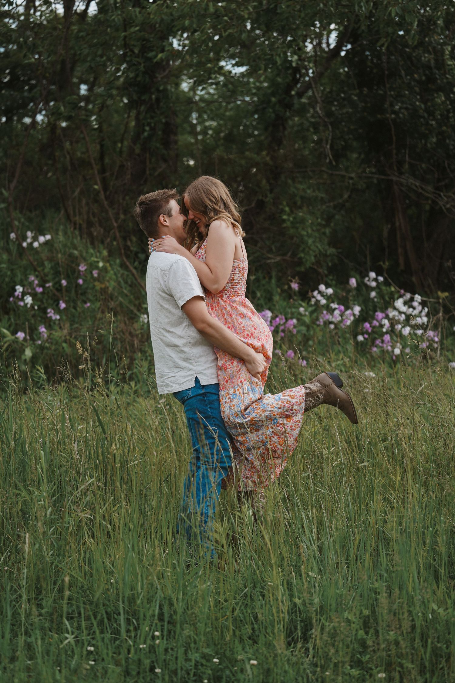 A romantic couple embraces in a field of tall grass and wildflowers during a summer photo session.
