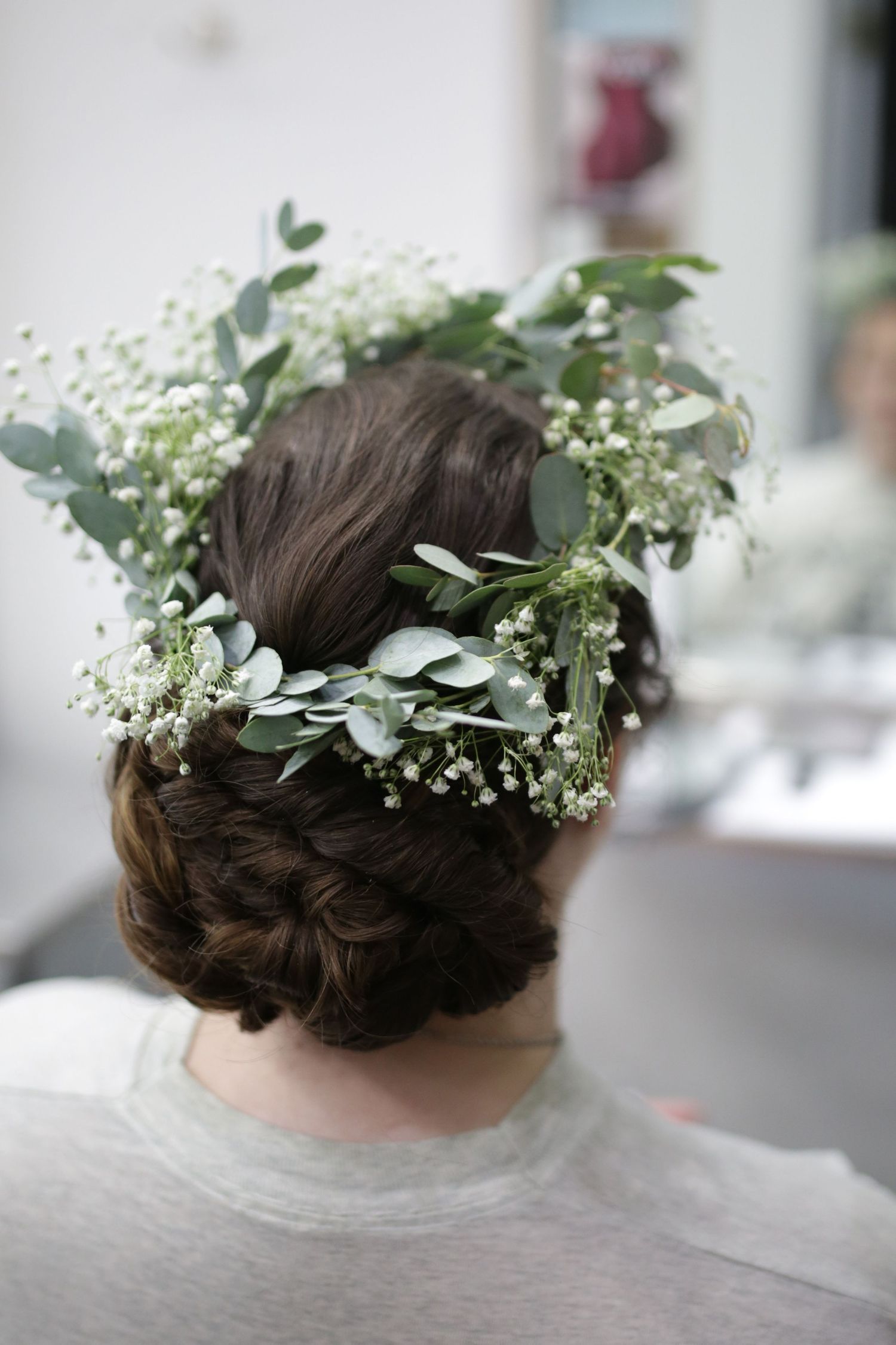A delicate floral crown made of baby's breath and eucalyptus leaves adorns an elegant braided updo hairstyle.