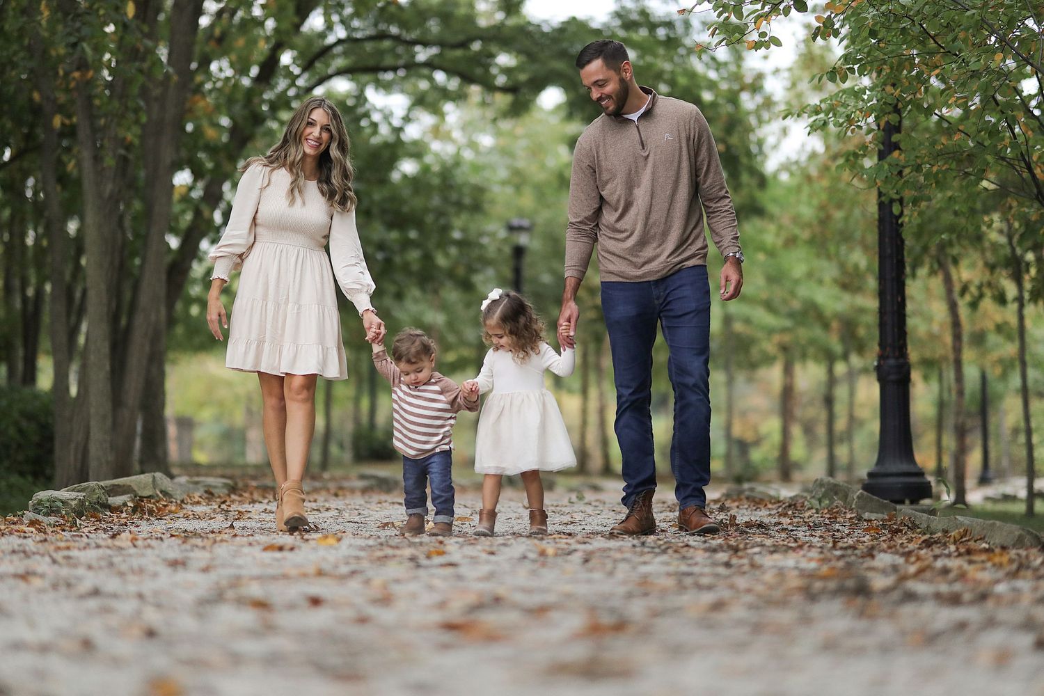 Family of four walking hand in hand on tree-lined path covered in fall leaves.  Family Photography in Strongsville Ohio