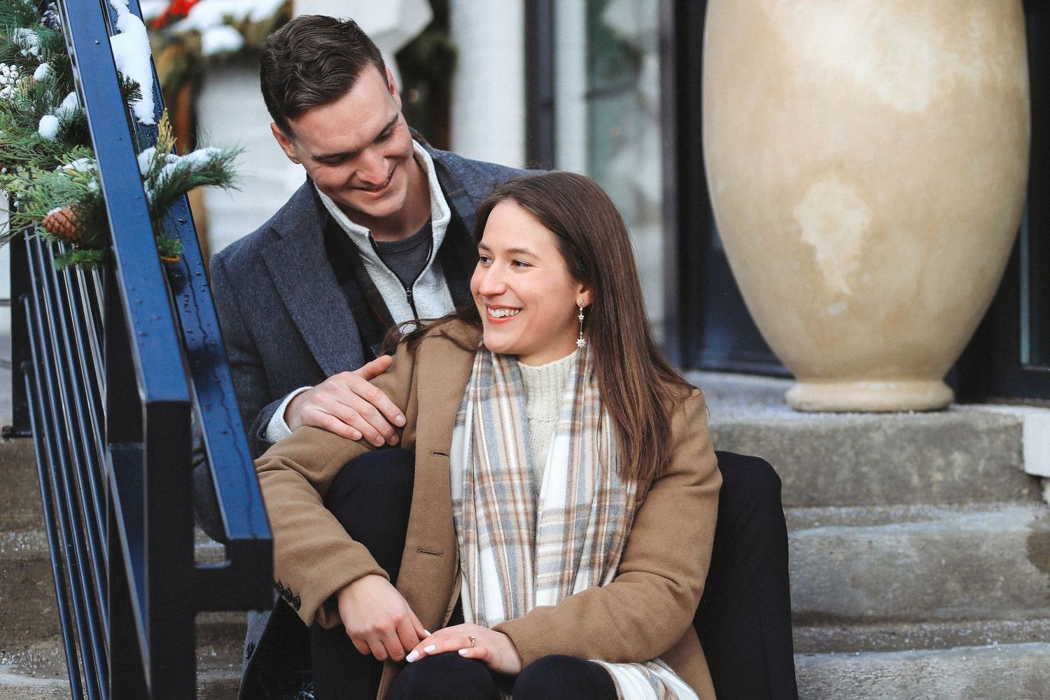 A couple in formal attire shares a joyful moment together on outdoor steps with large decorative urns.