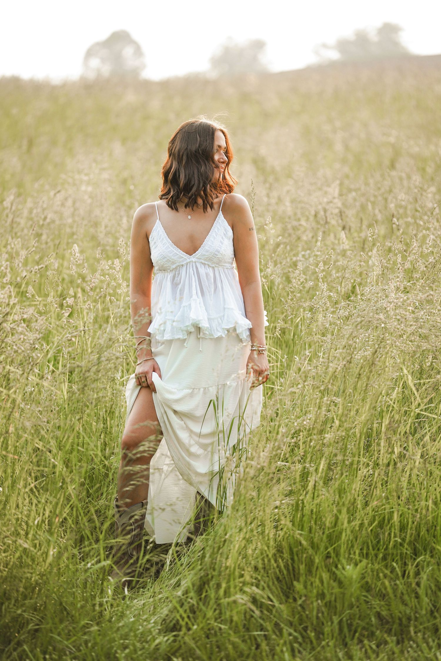 Person in white flowing dress standing in tall grass meadow at golden hour.