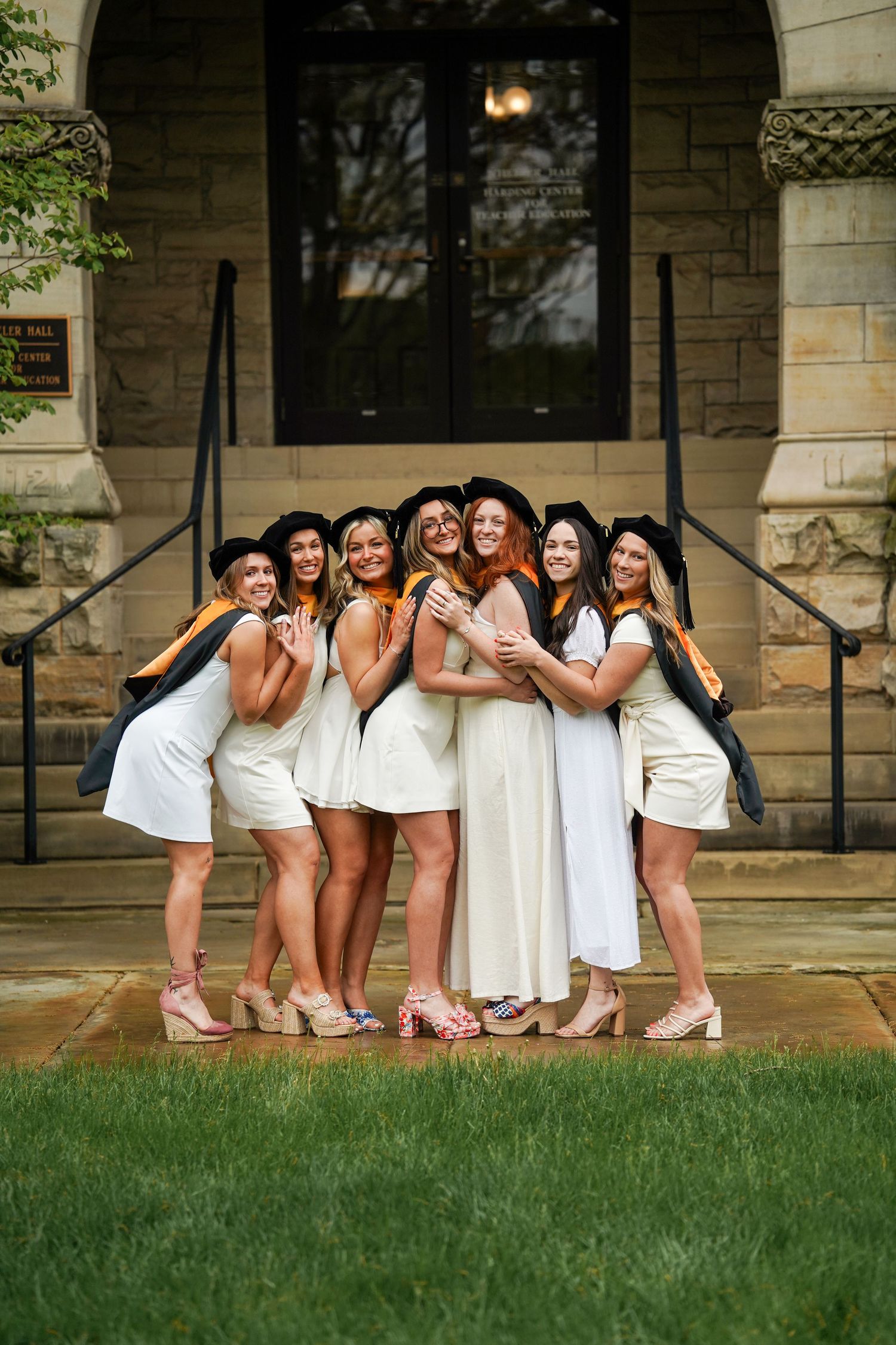 A group in white dresses poses together on stone steps during a sunny outdoor photoshoot.