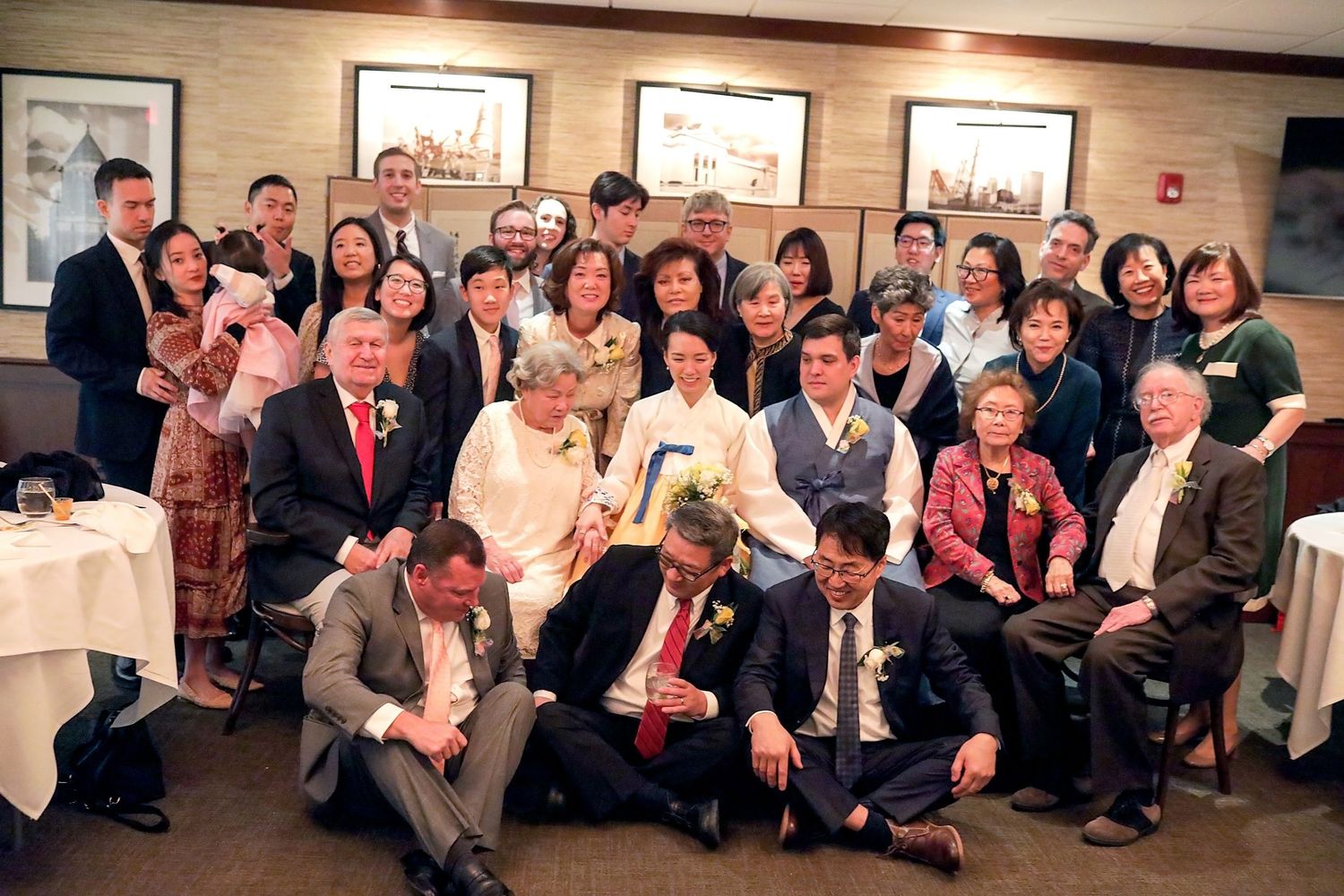 A large group of wedding guests gathered in a long panoramic shot of what appears to be a reception venue.