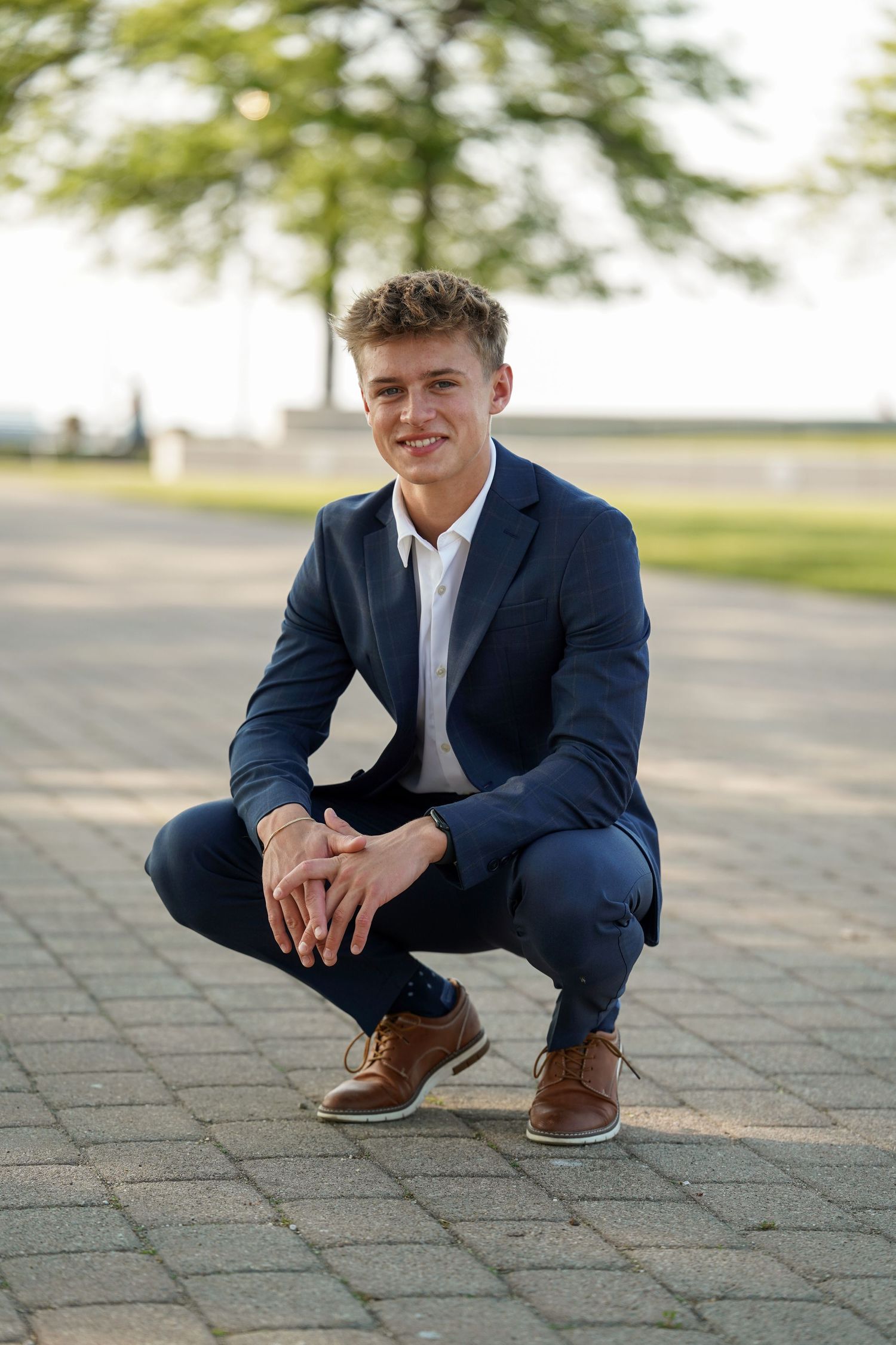 A person in a navy suit and white shirt crouches down on paved stone ground in three similar poses.