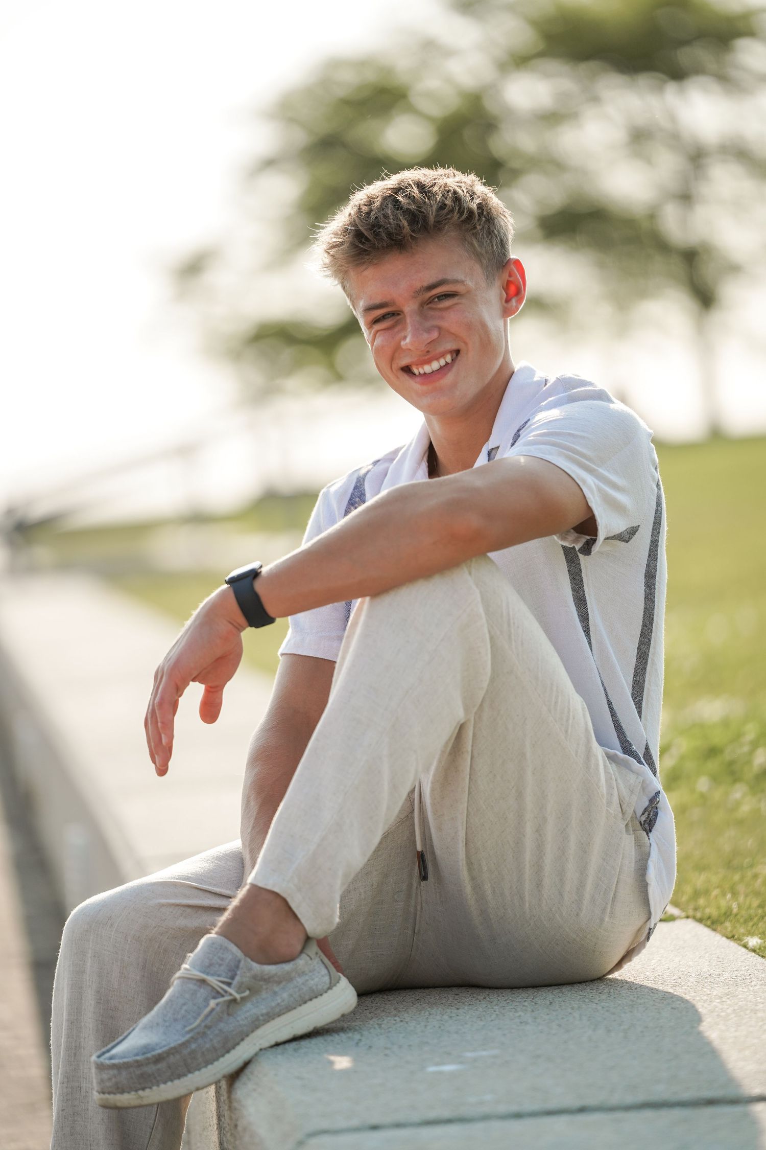 Person wearing casual white outfit with sneakers sits on concrete ledge outdoors during golden hour.