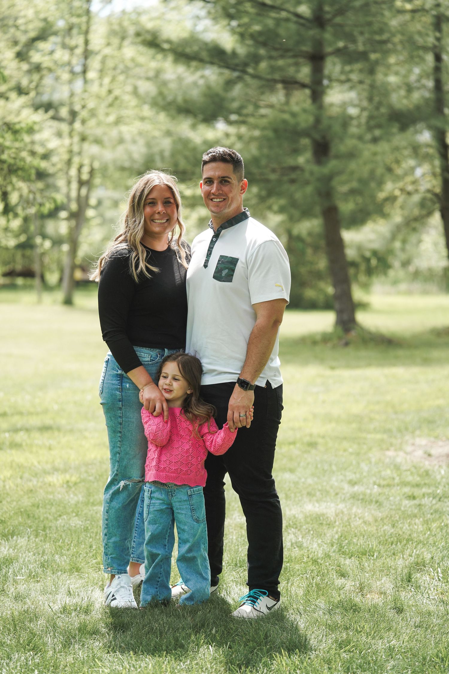 Family wearing matching outfits poses together in a grassy field with green trees in the background.