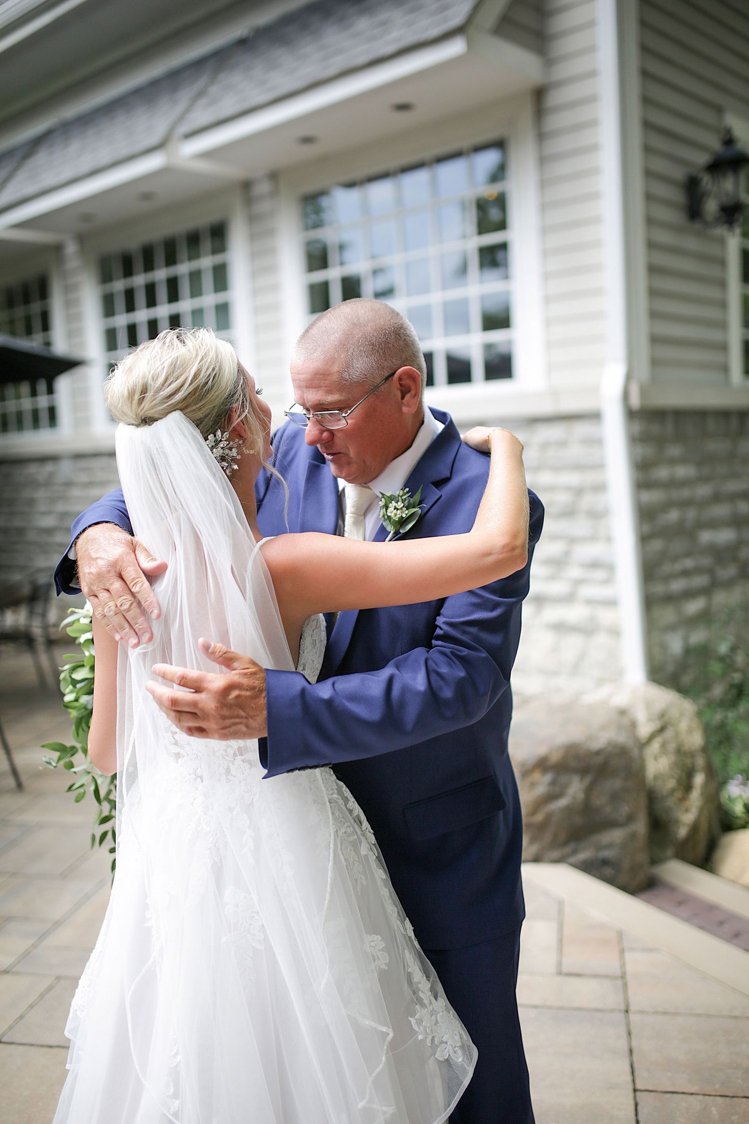 An emotional first look moment takes place outside a white house with stone accents.