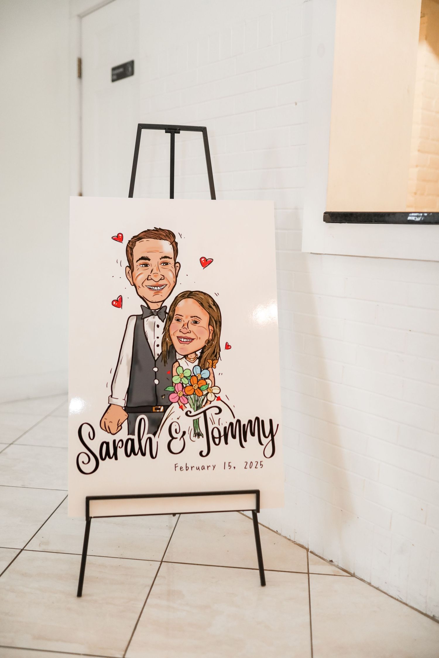 Custom illustrated wedding portrait displayed on white easel with decorative hearts and calligraphy text.