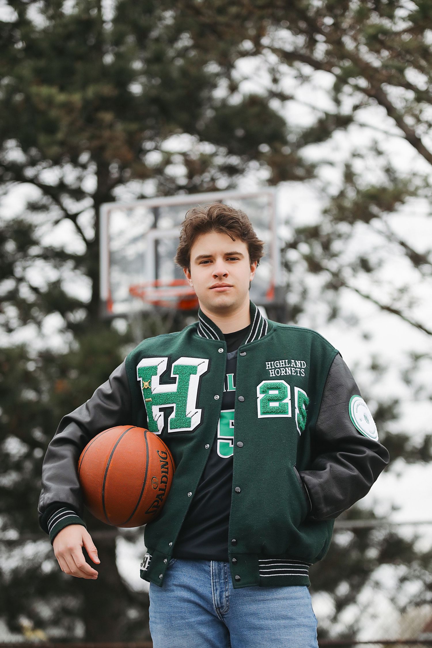 A basketball player in a green varsity jacket and jeans poses with a basketball in a series of outdoor shots.