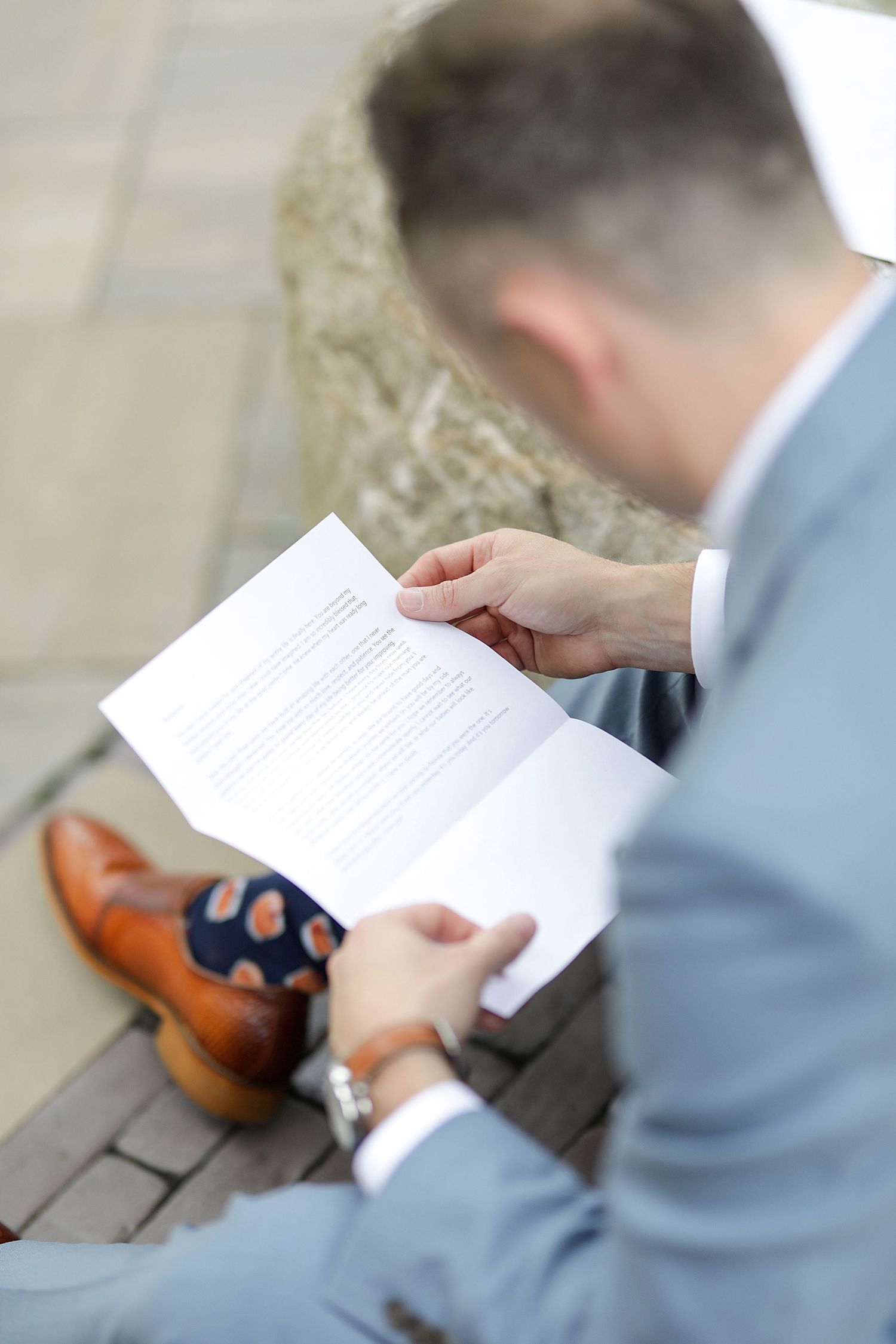 Close up of groom reading letter while wearing light blue suit with brown leather shoes.