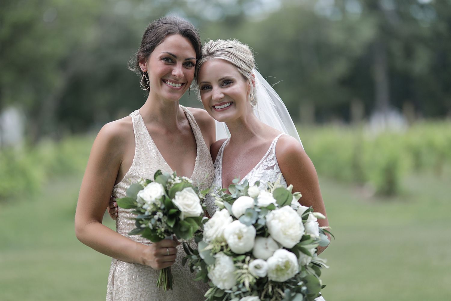 Wedding party members posing with white floral bouquets in an outdoor garden setting.