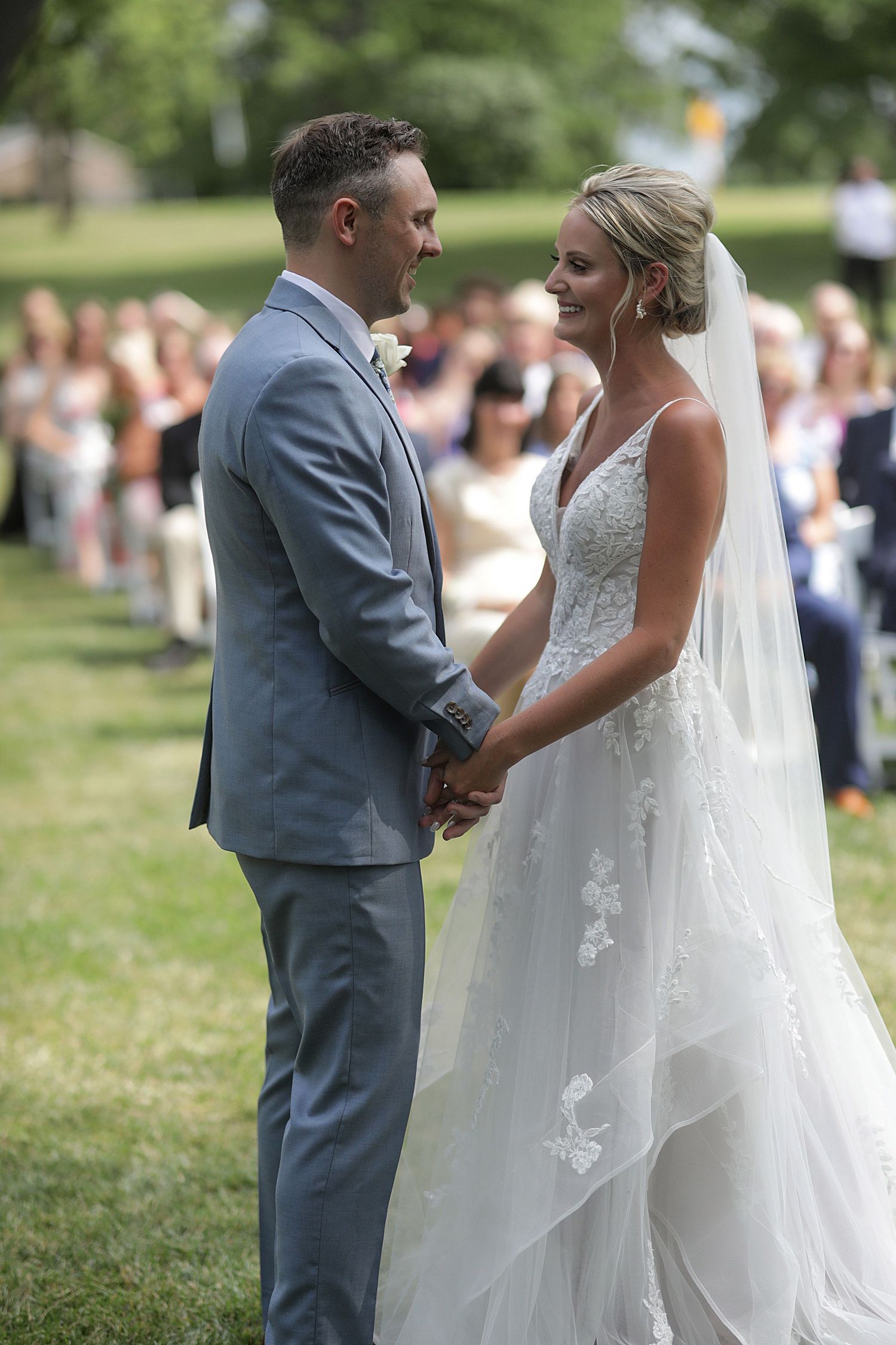 Couple sharing intimate outdoor wedding ceremony moment on grassy lawn.