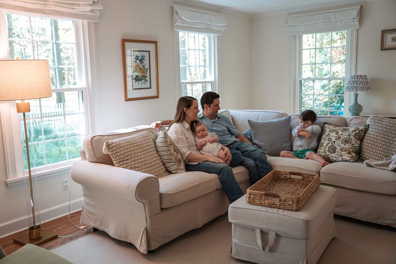 Family relaxes together in a cozy living room with white sofas, windows, and warm natural lighting.