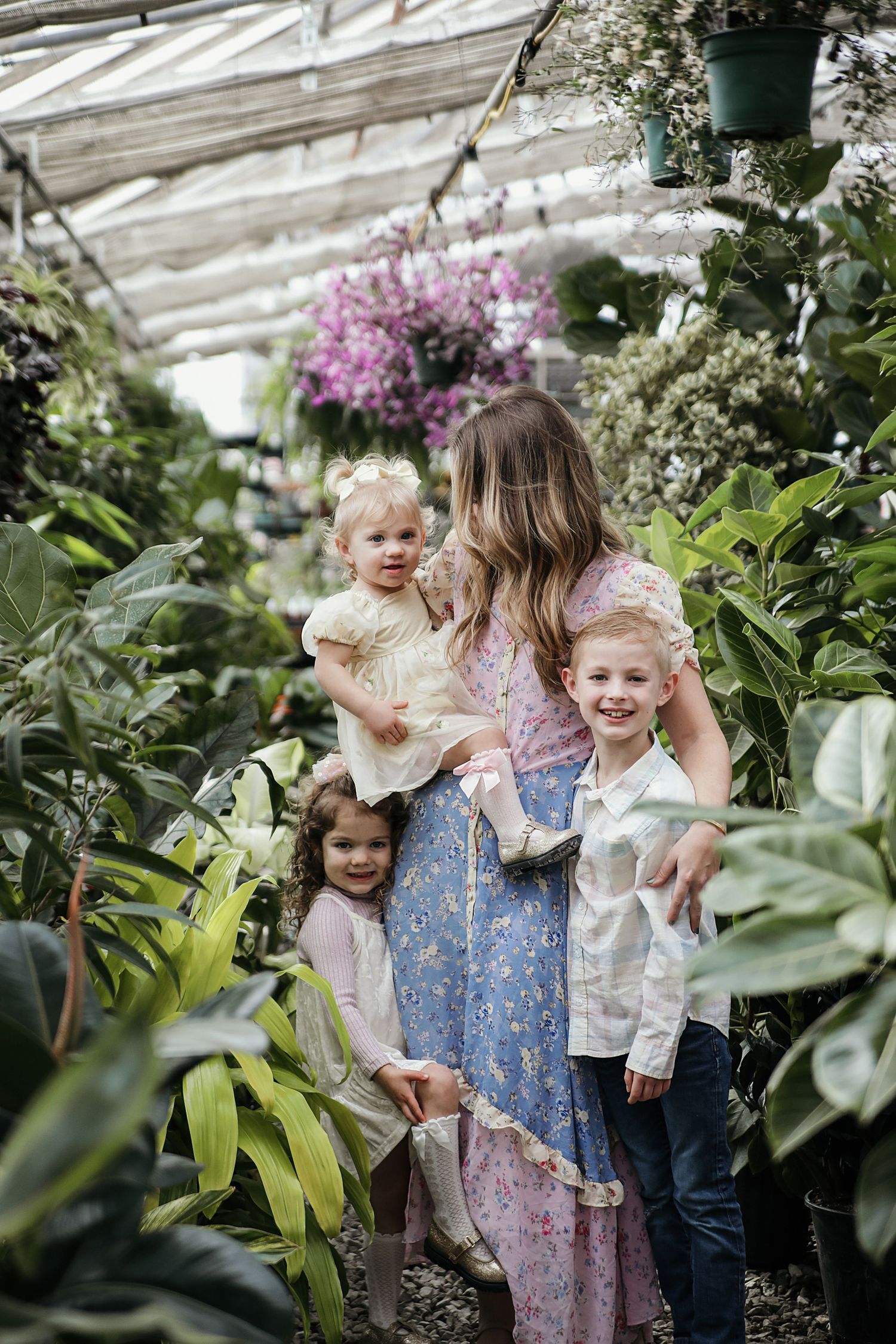 A floral greenhouse scene with a woman and children surrounded by lush plants and pink blooms.  Family Photography in Medina Ohio.