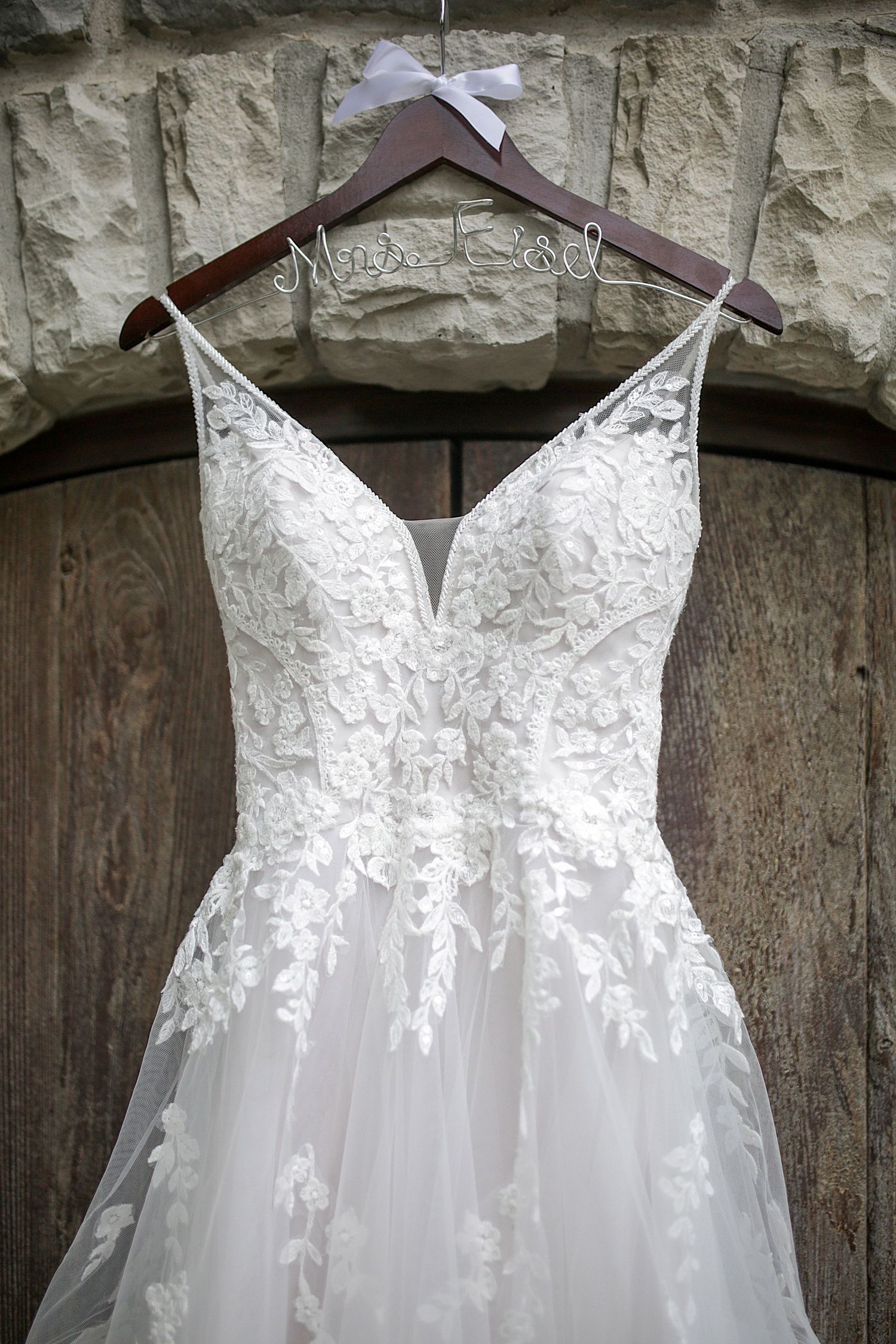 An elegant white lace wedding dress with v-neckline hanging on display against a stone wall. Wedding Photographer in Cleveland Ohio