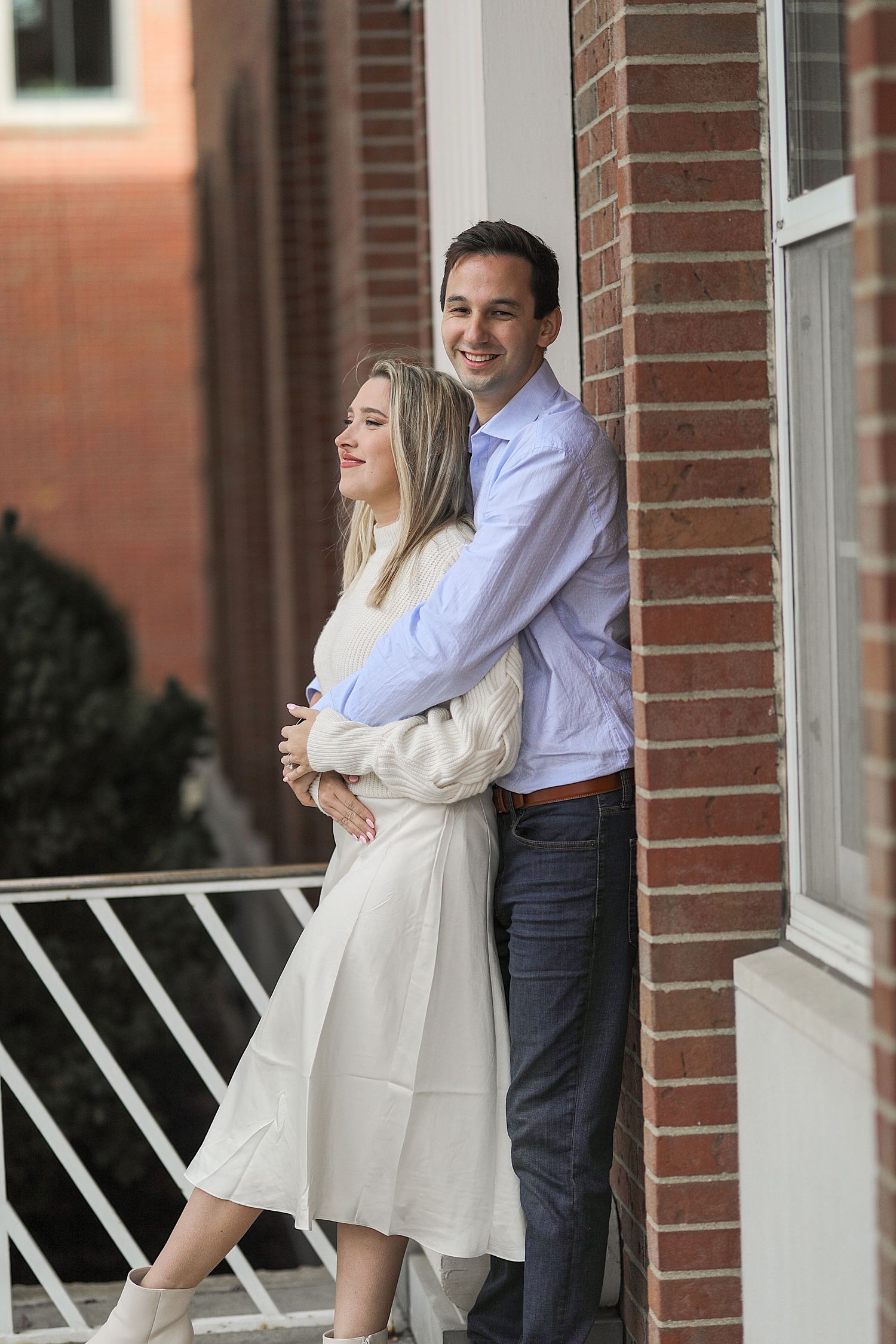 A couple in monochromatic outfits shares multiple romantic moments on a brick-lined porch.