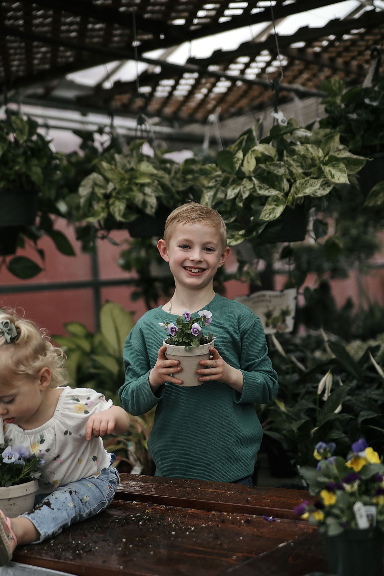 Young children in a greenhouse helping with potted plants and gardening activities.