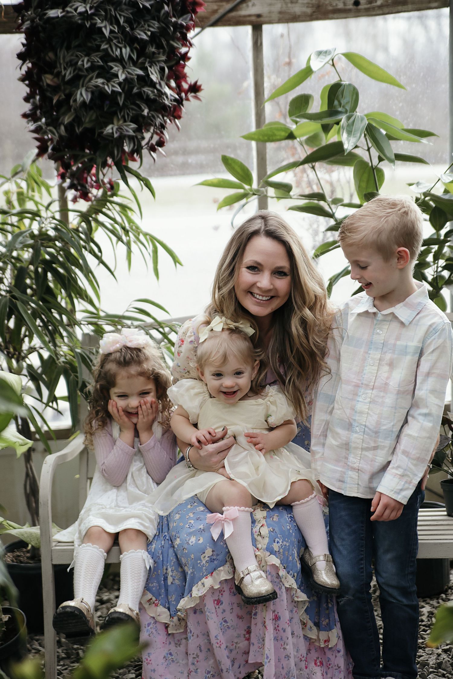 A family shares joyful moments while posing together in front of green plants and windows in a casual photo session.
