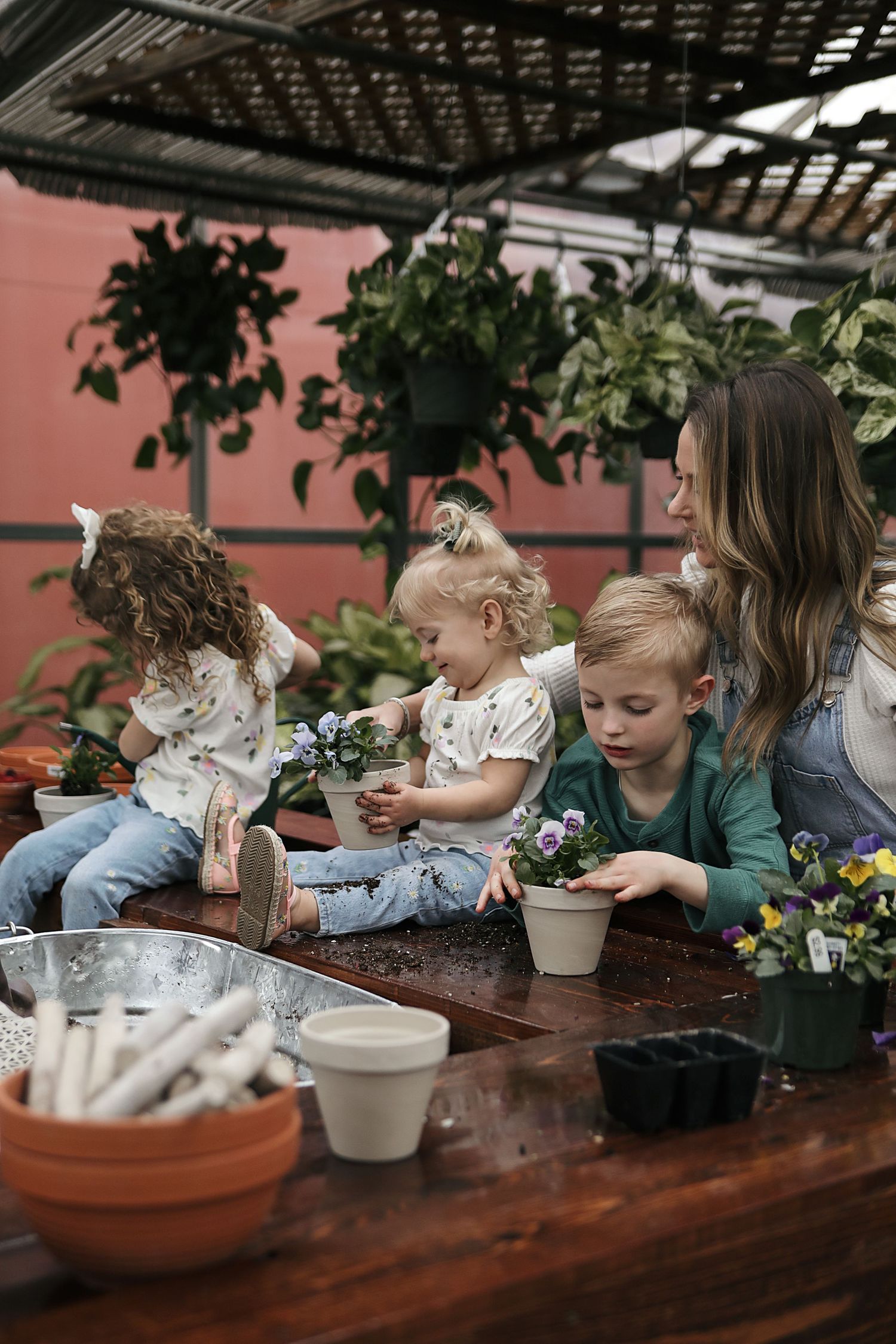 Children engage in planting and gardening activities at a wooden table with terracotta pots and potting supplies.