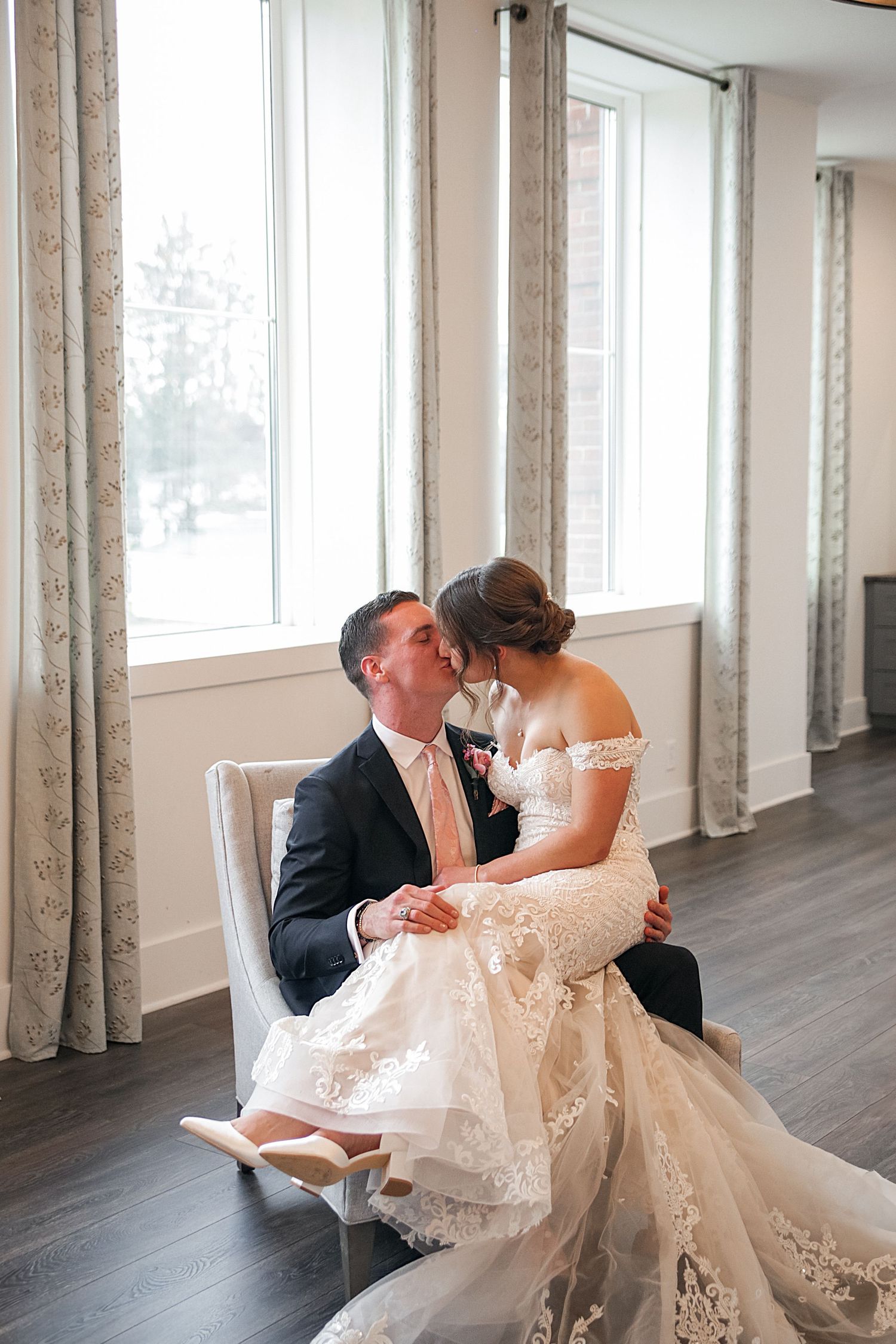 A romantic moment between newlyweds in a bright, modern room with white curtains and hardwood floors.