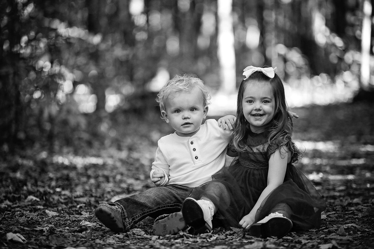 Two children sitting together in forest setting captured in black and white photography.  Family Photography in Medina Ohio.