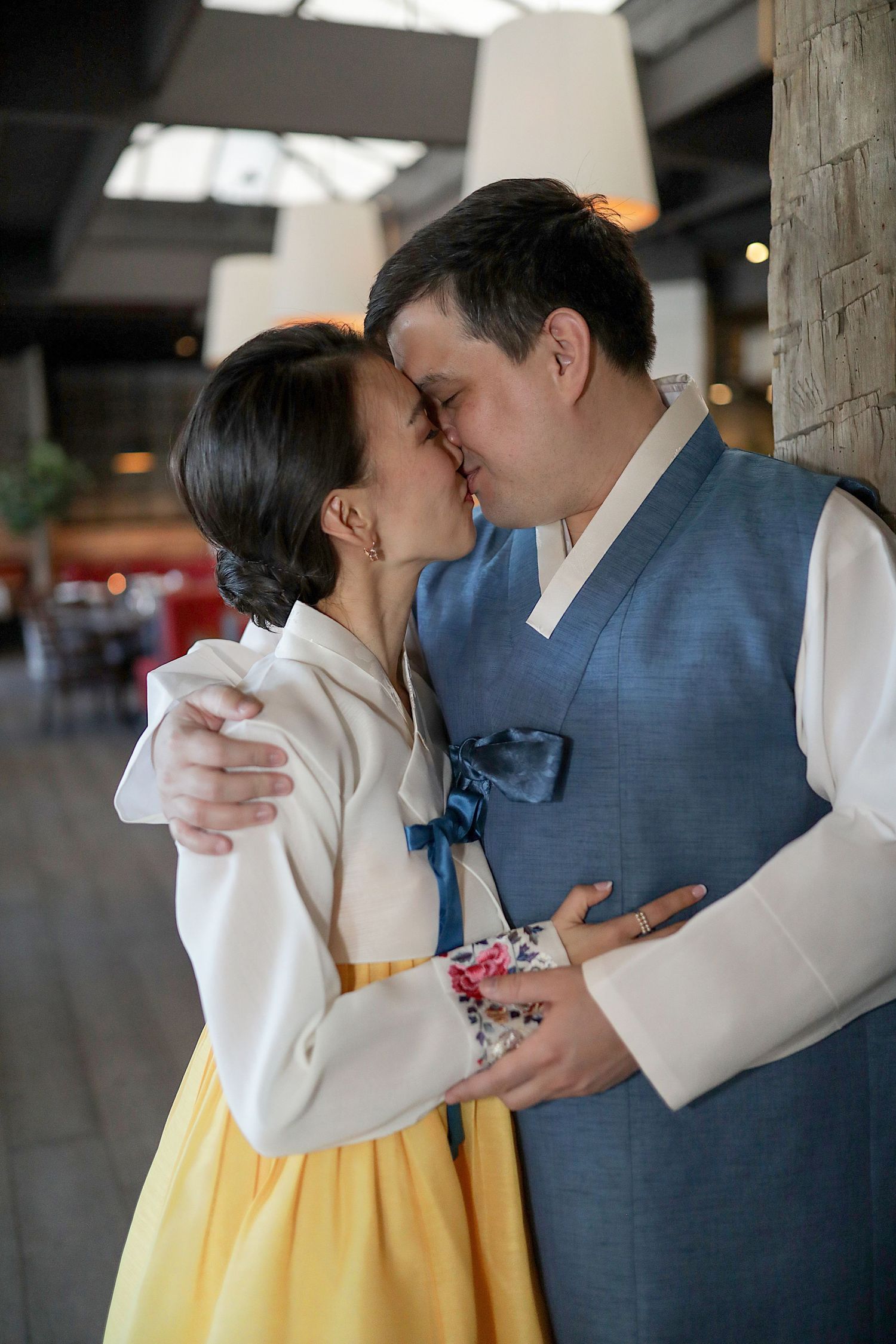 A couple wearing traditional Korean hanbok share a romantic kiss while holding each other.