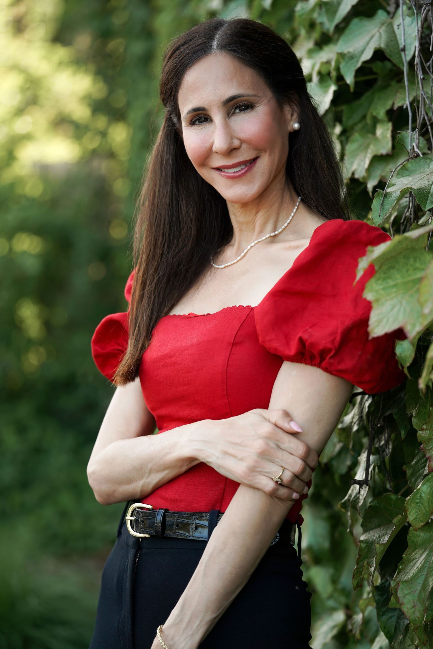 Woman in red puff sleeve top and black skirt poses against green foliage in outdoor portrait series.