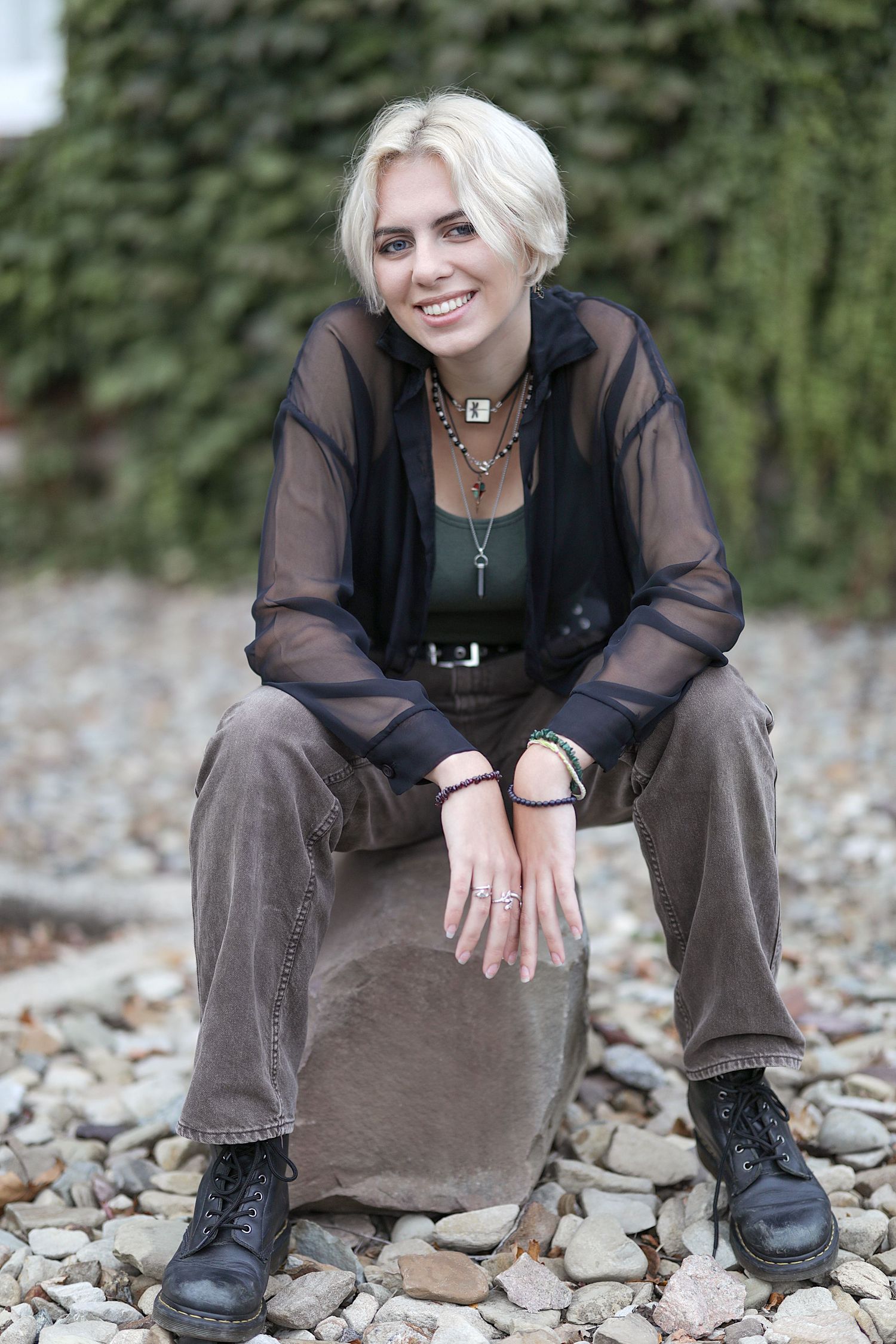 Person in casual brown clothing sits on rocks while sharing a candid smile in an outdoor setting.