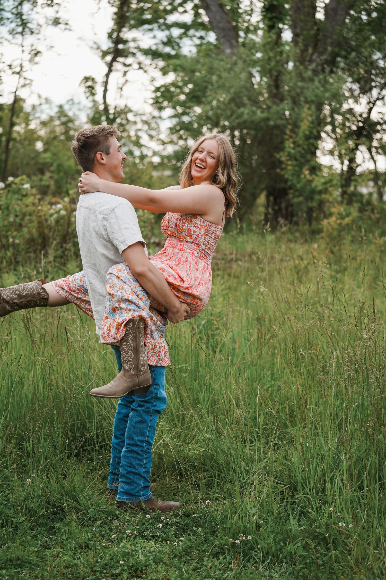 A romantic couple shares a joyful moment in tall grass as the man lifts his partner in a playful embrace.