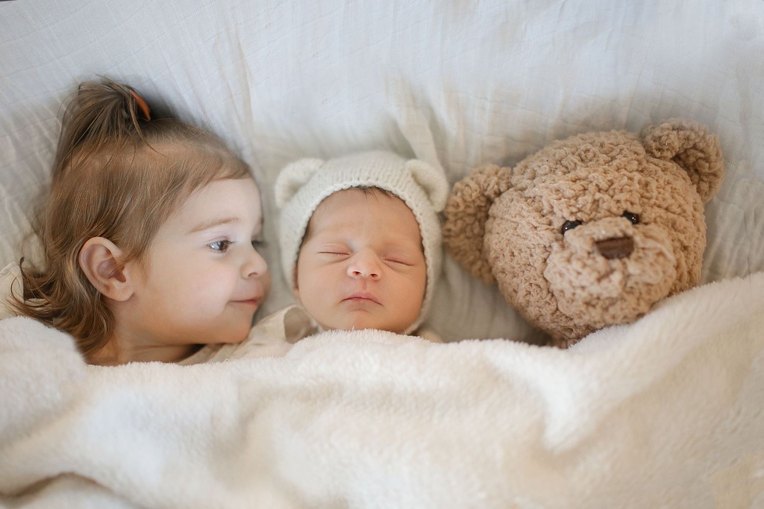 A collage of four images showing sleeping babies with a teddy bear resting on soft white bedding.