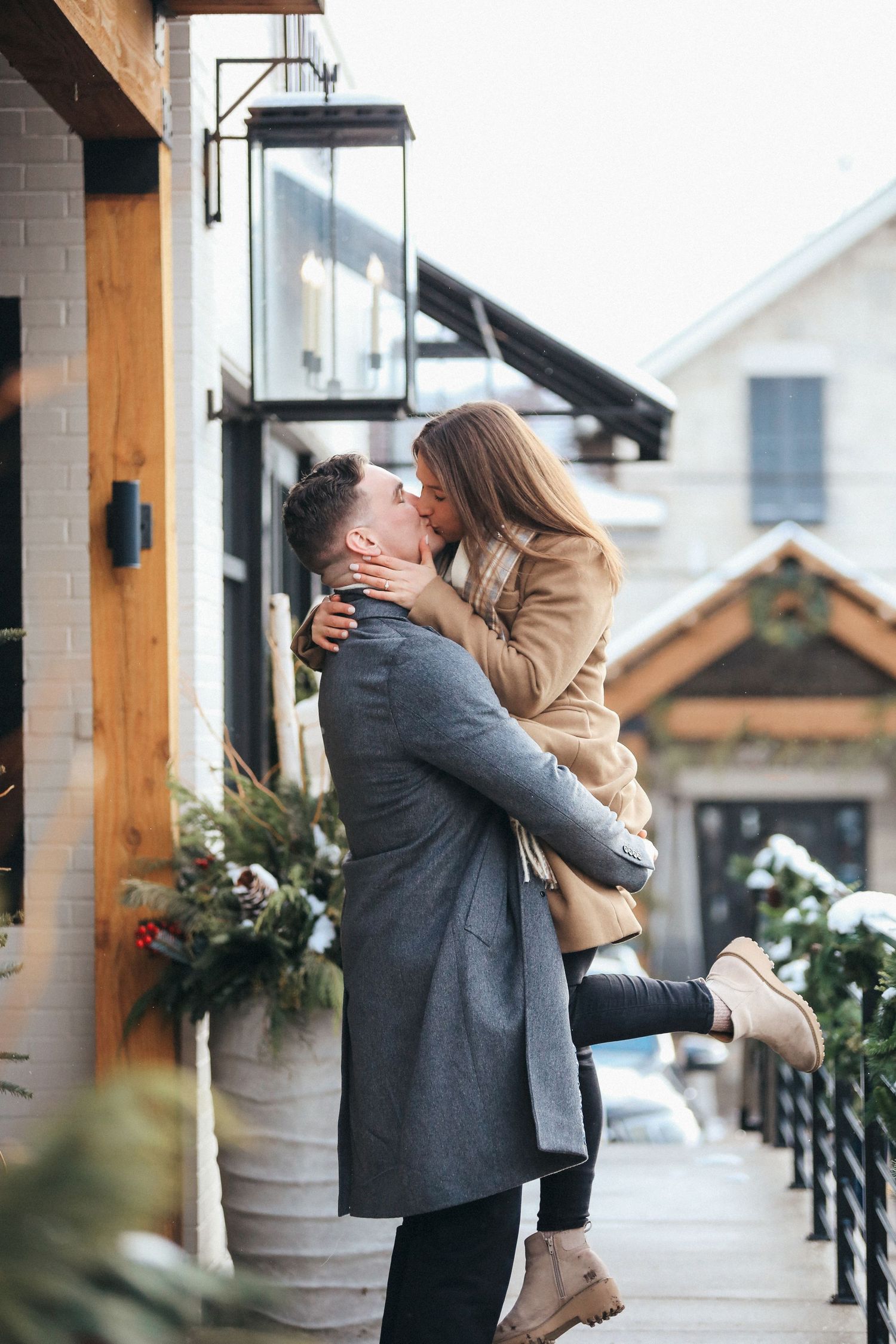 Couple embraces and shares romantic moment on outdoor porch with rustic wooden beams and winter decor.