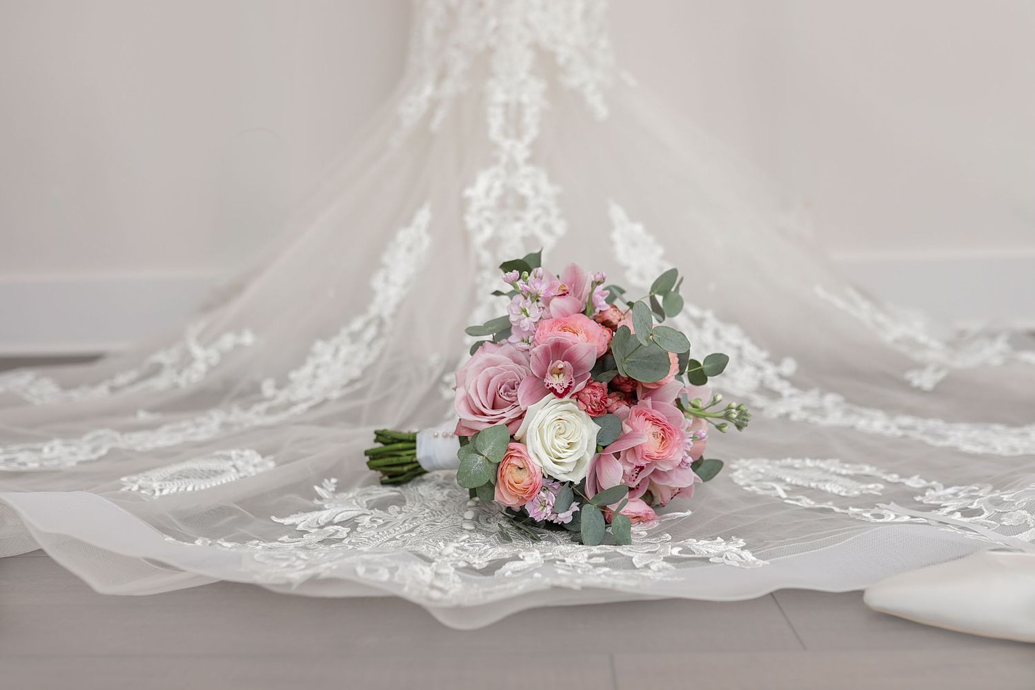 Delicate white lace wedding veil with floral embroidery details draped elegantly against a light background.