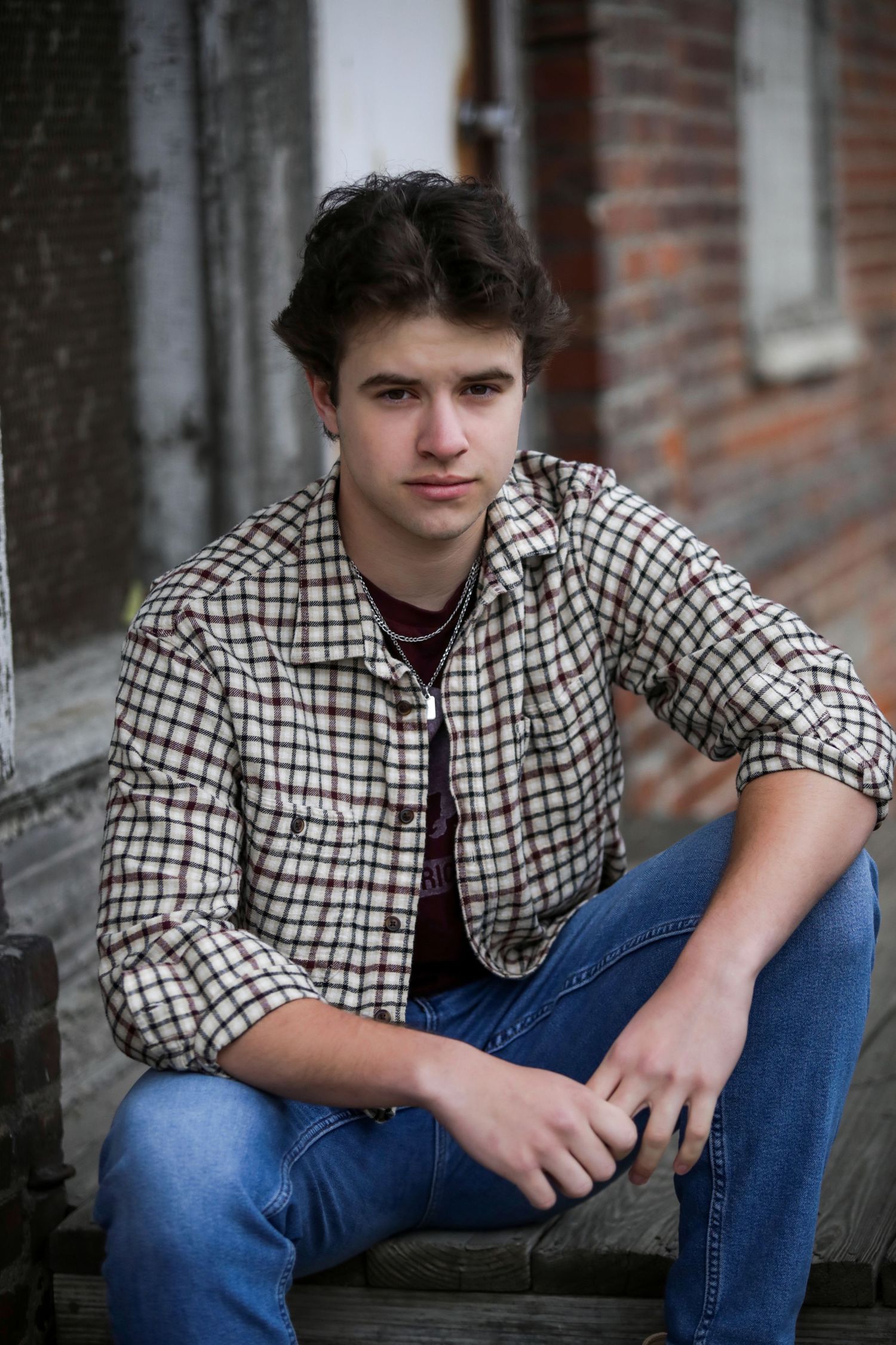A person in a checkered shirt and jeans poses against a brick wall in a series of casual portraits.