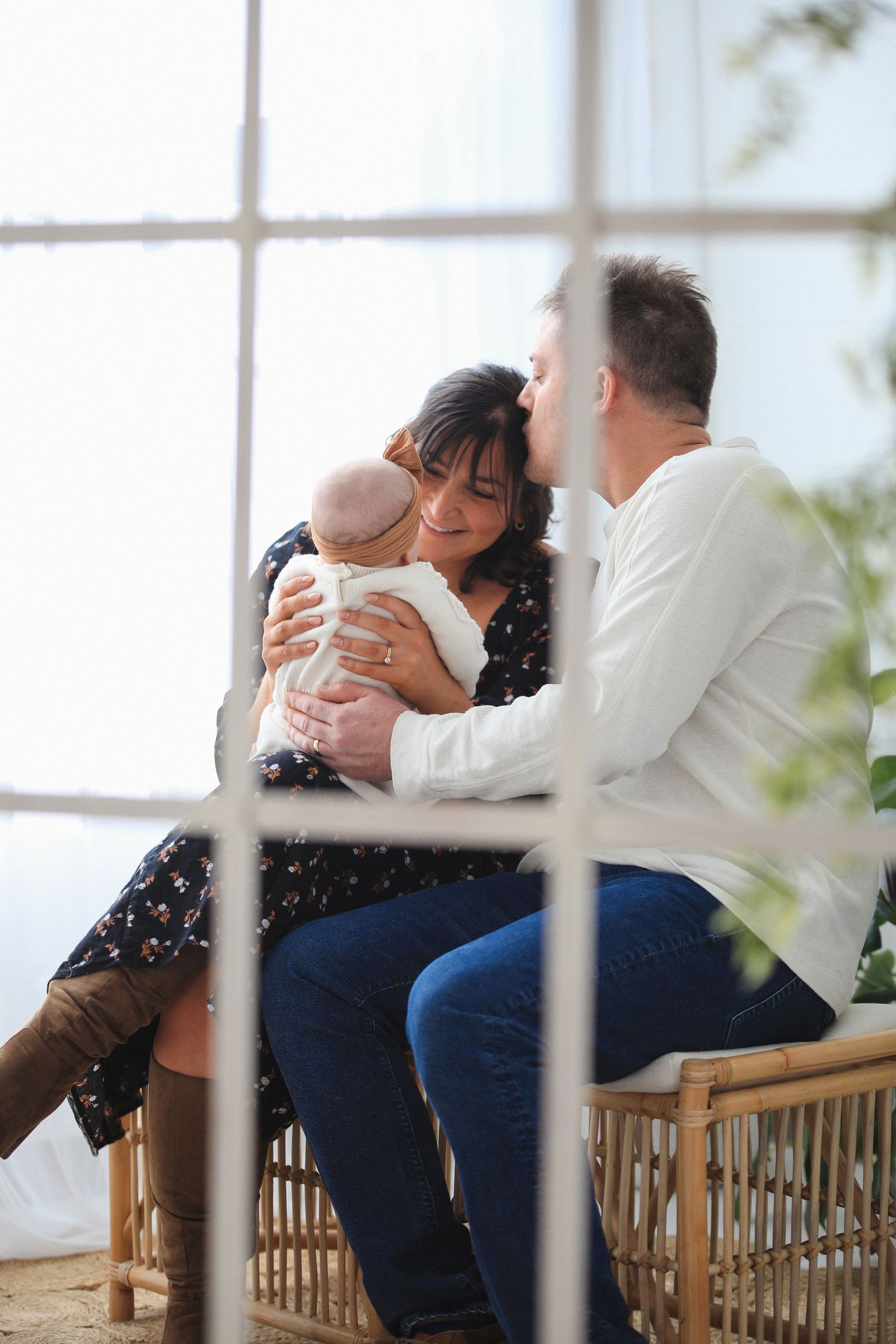 A couple sits close together on a wooden bench sharing an intimate emotional moment by a window.