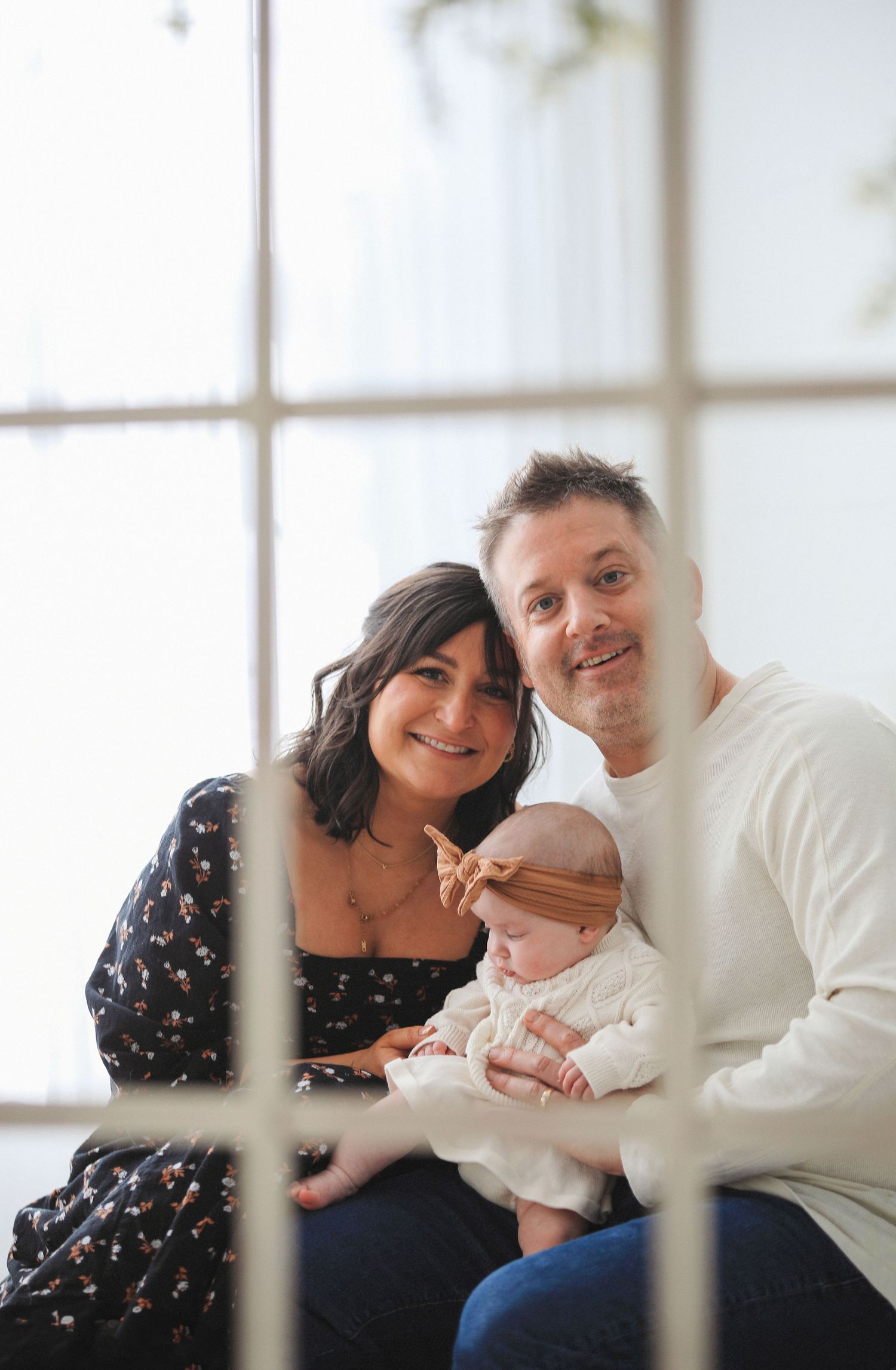 A family poses together on a bench near bright windows in a series of loving interactions.