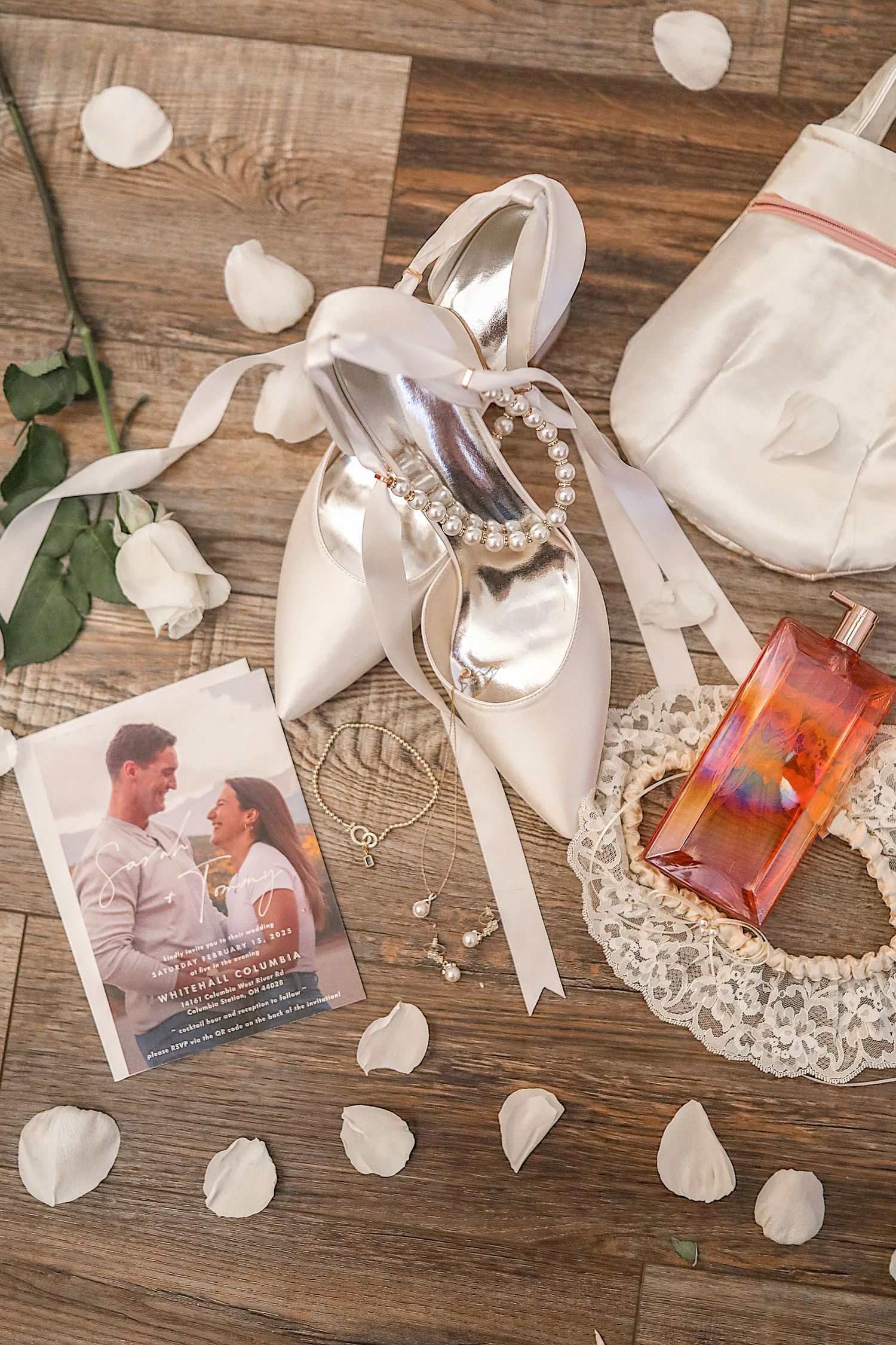 Wedding photos and decorative items arranged on rustic wooden surface with white rose petals and lace doilies.