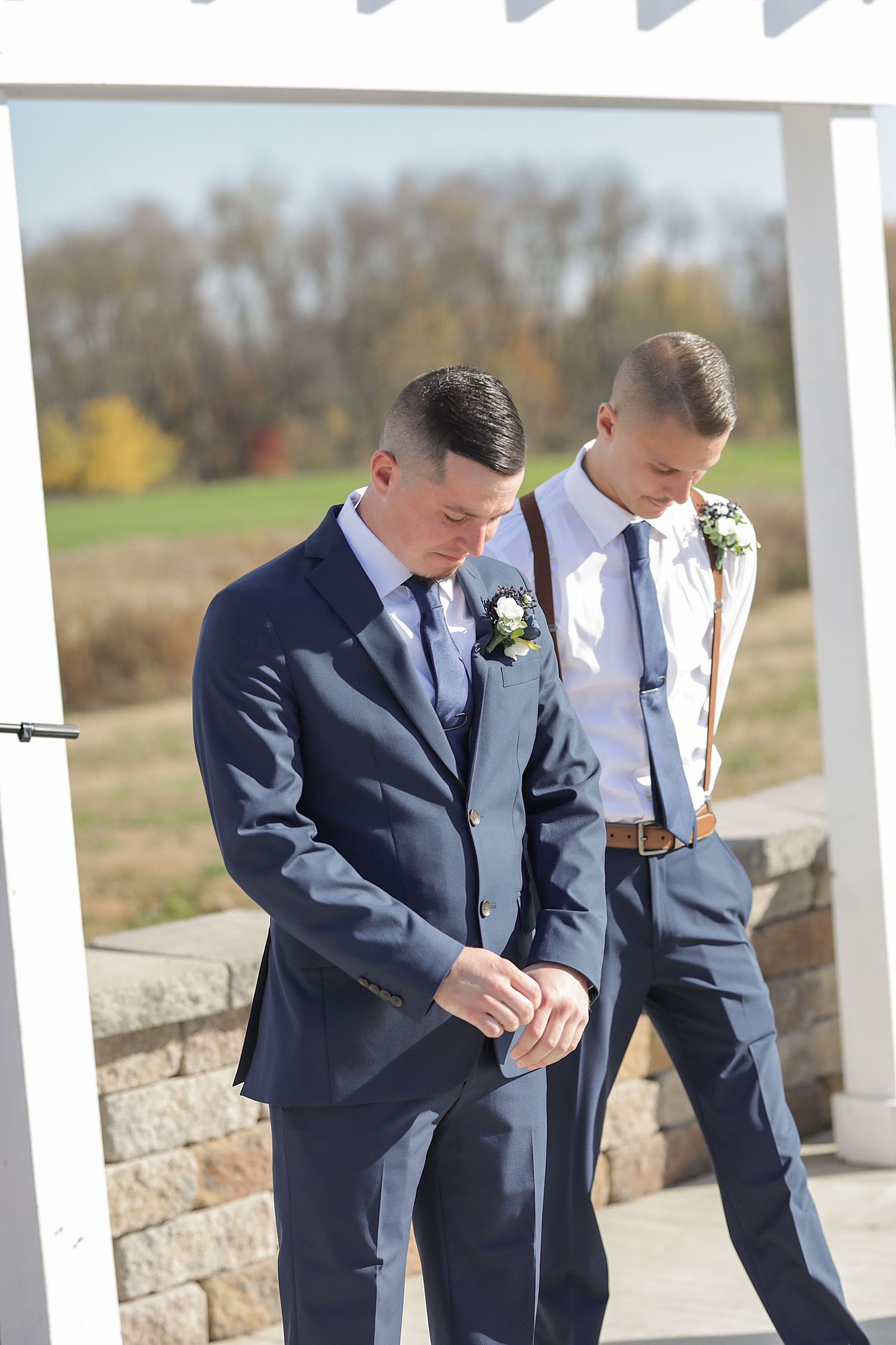 Wedding party in navy suits looking down at something during outdoor photo session.
