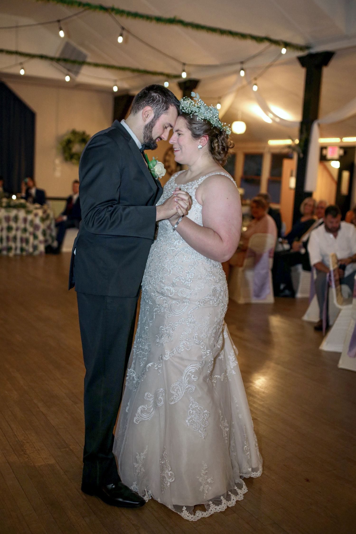 A couple shares their first dance as newlyweds on a wooden dance floor under twinkling string lights at their reception.